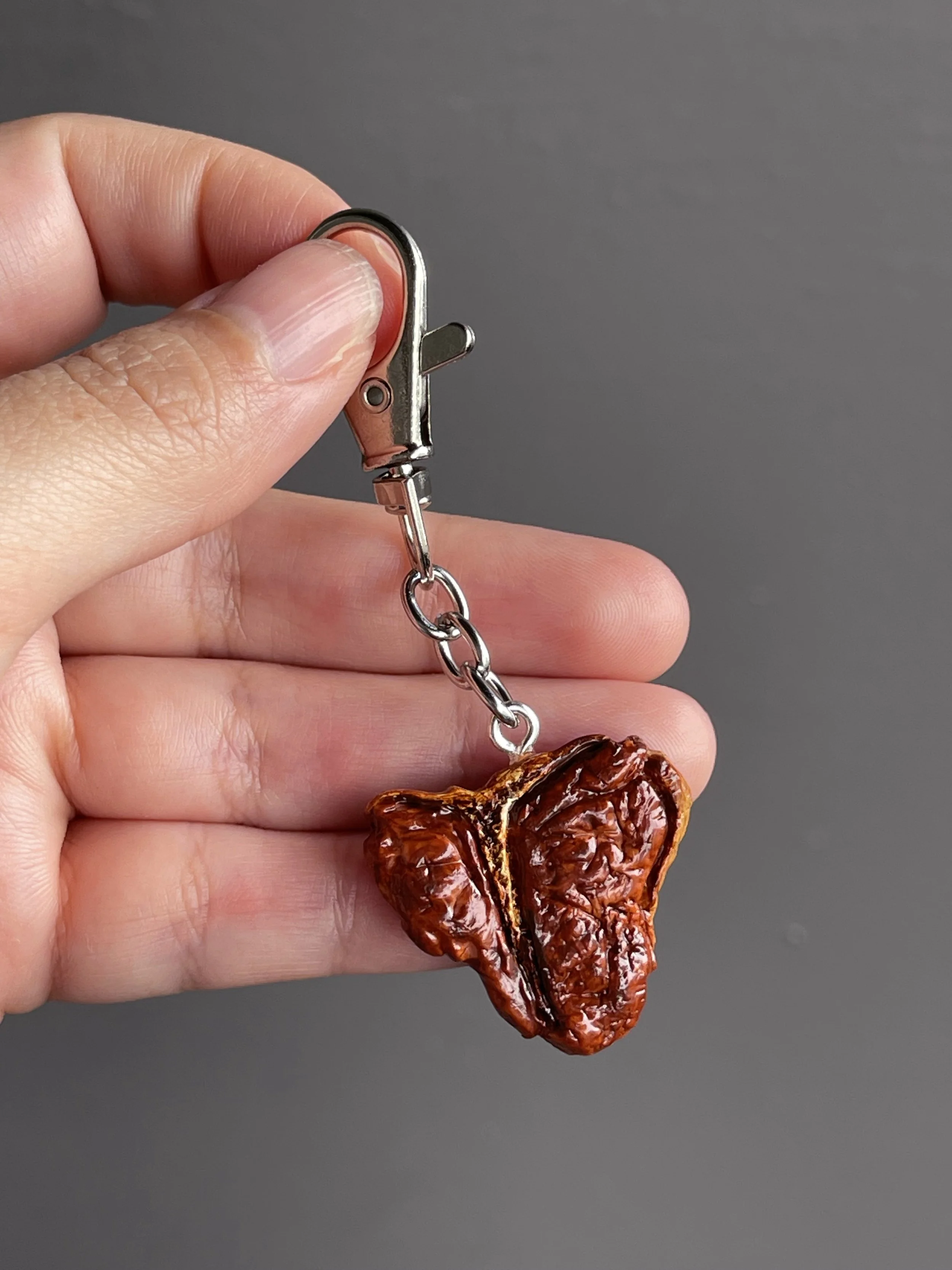 A hand holding a realistic miniature polymer clay t-bone steak keychain.
