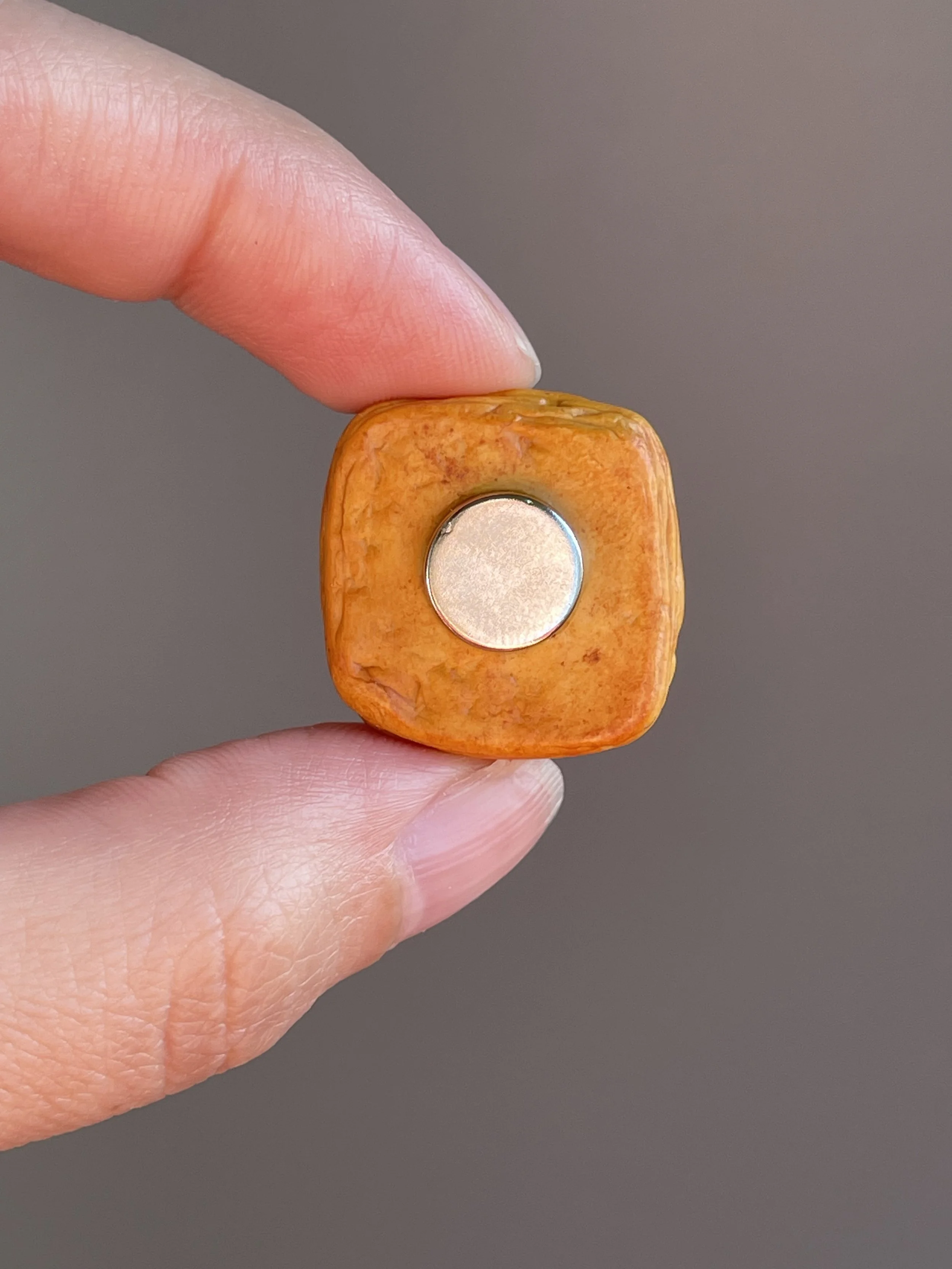 Fingers holding a miniature polymer clay egg, tomato, jalapeño breakfast danish magnet showing the back.