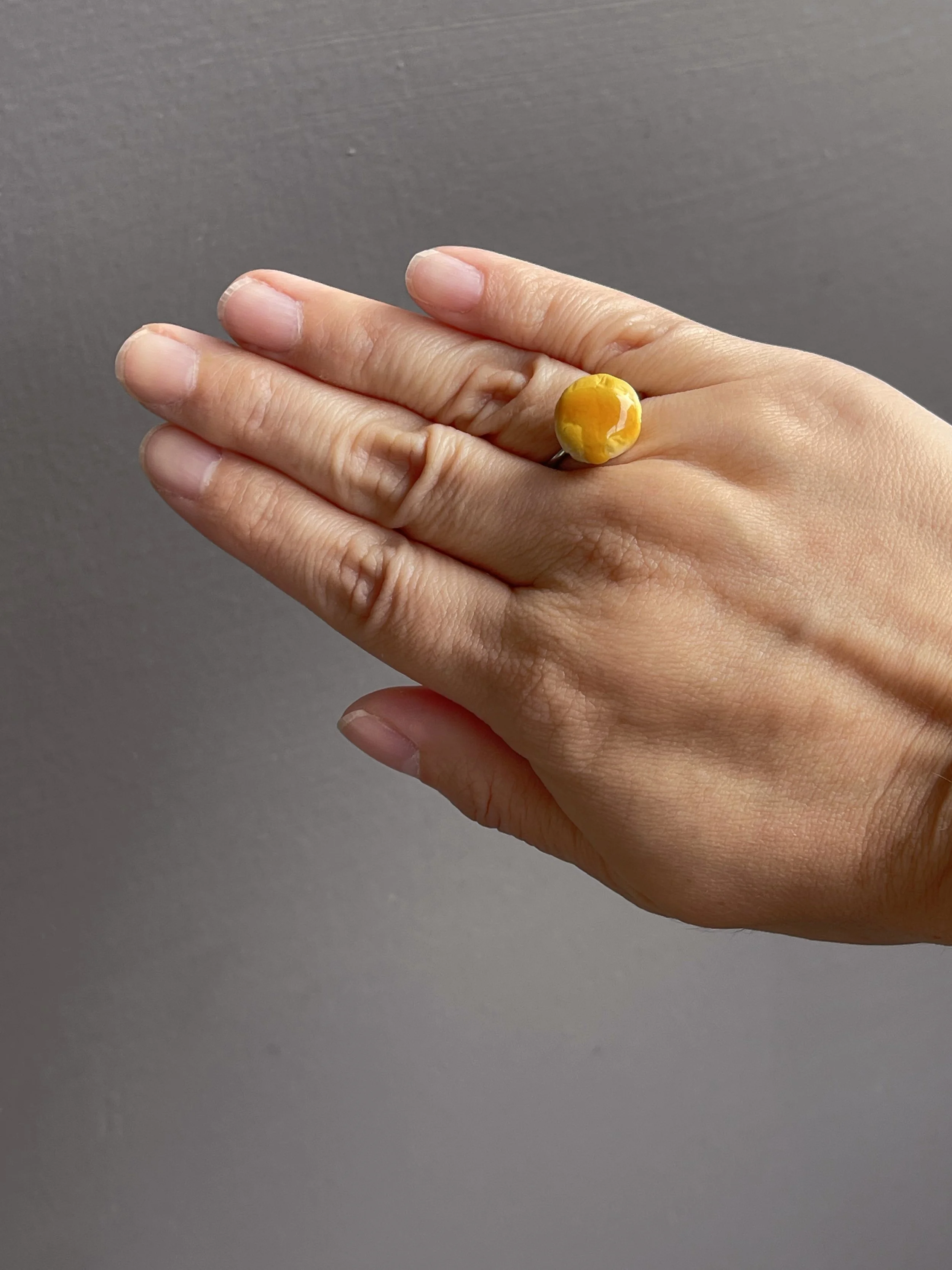 A hand wearing an adjustable ring topped with a miniature polymer clay biscuit with resin dripping honey.