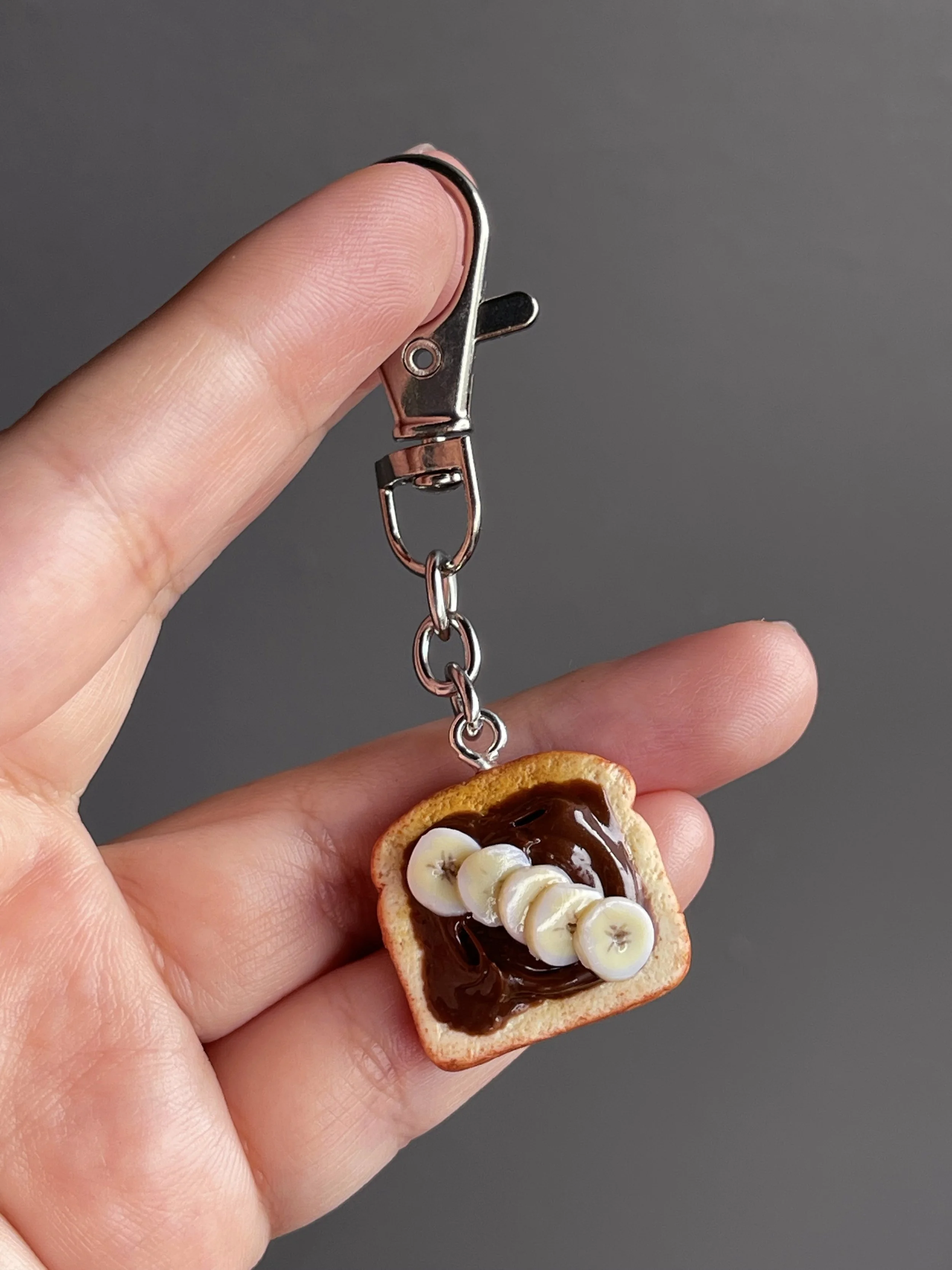 A hand holding a miniature polymer clay toast with hazelnut spread and banana slices.