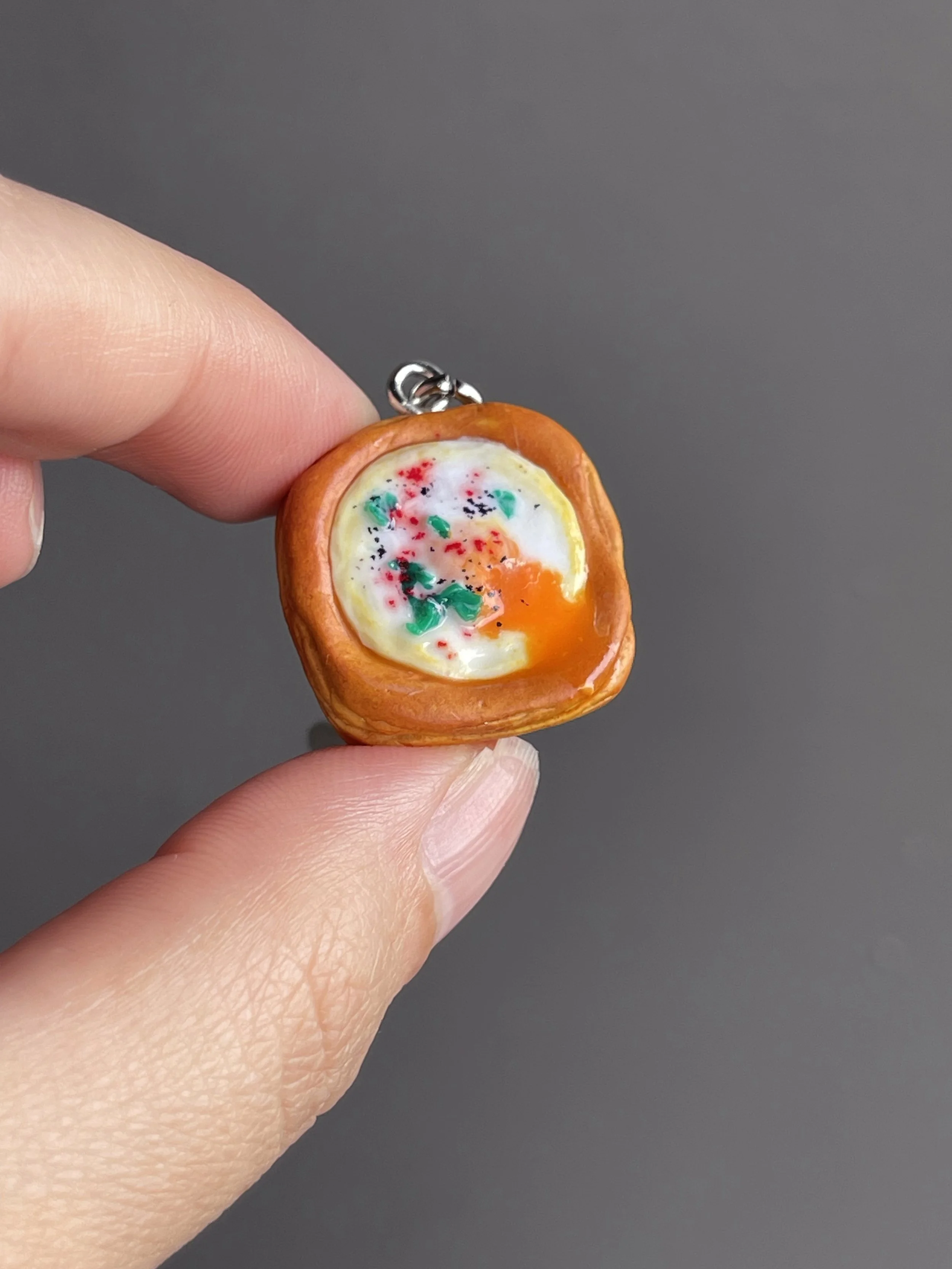 A hand holding a miniature polymer clay egg danish keychain with runny egg yolk.