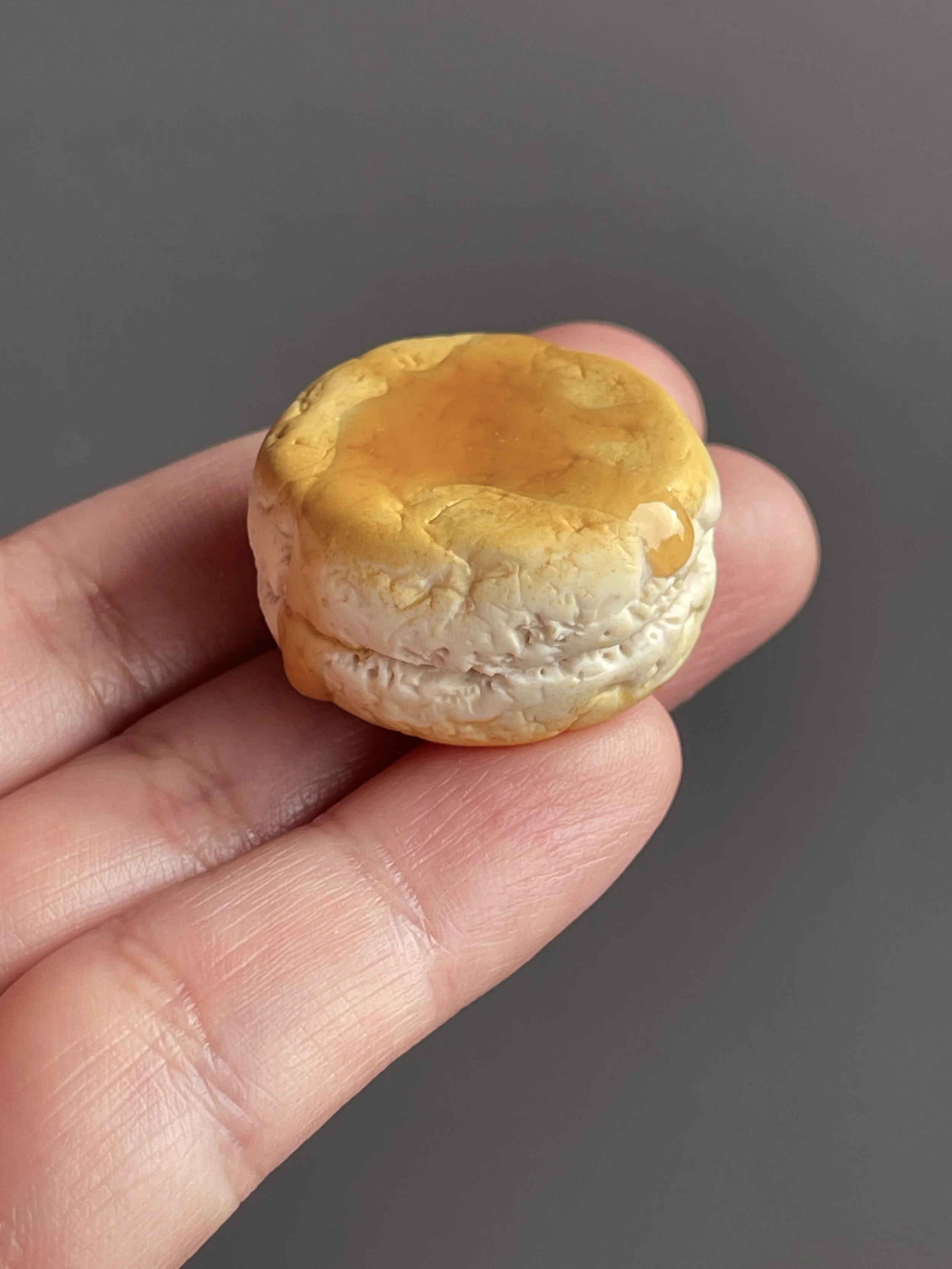 A hand holding a polymer clay biscuit and honey magnet.