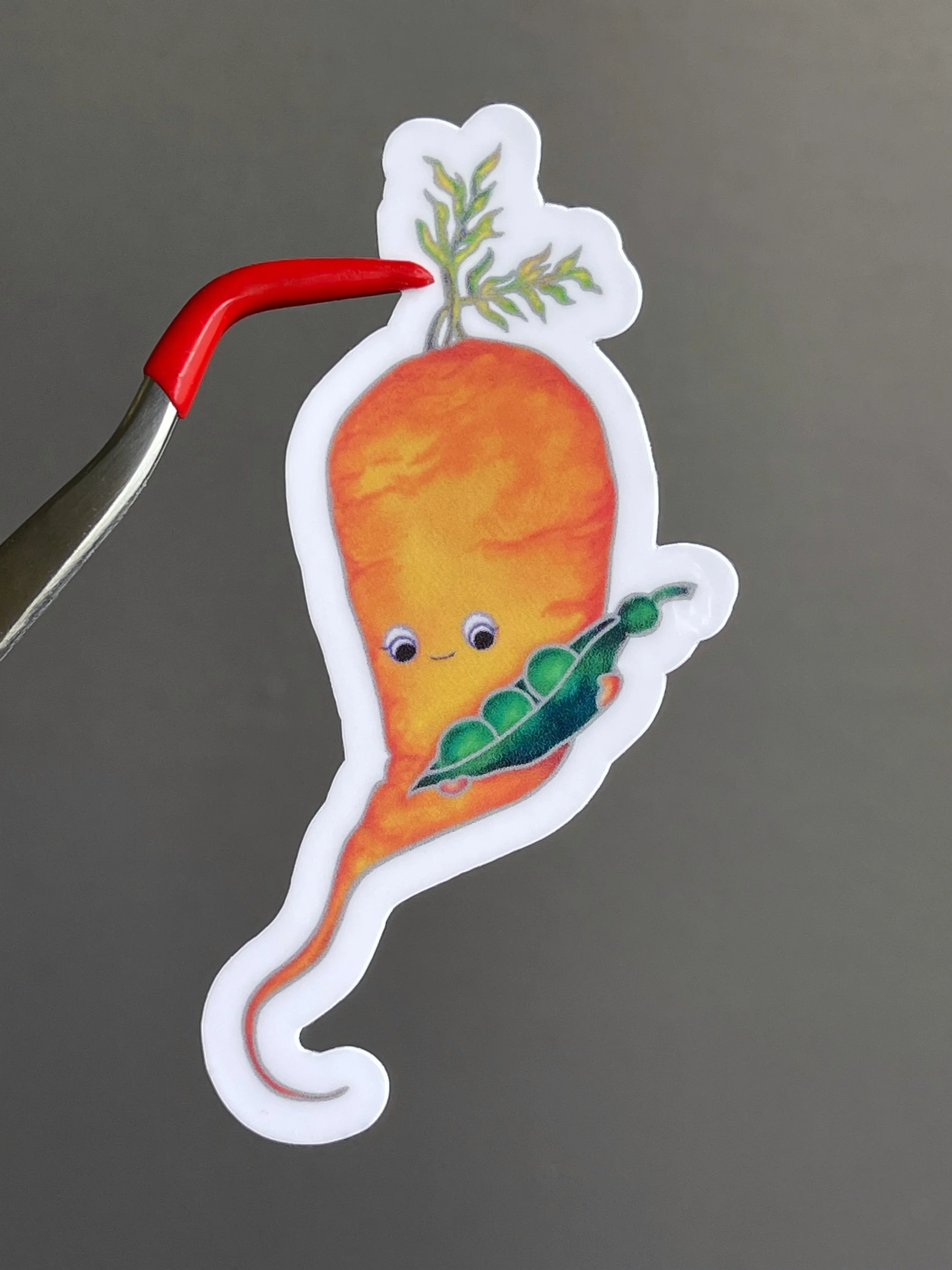 Red tip bent tweezer holding a sticker of a cute carrot character holding an open pea pod.