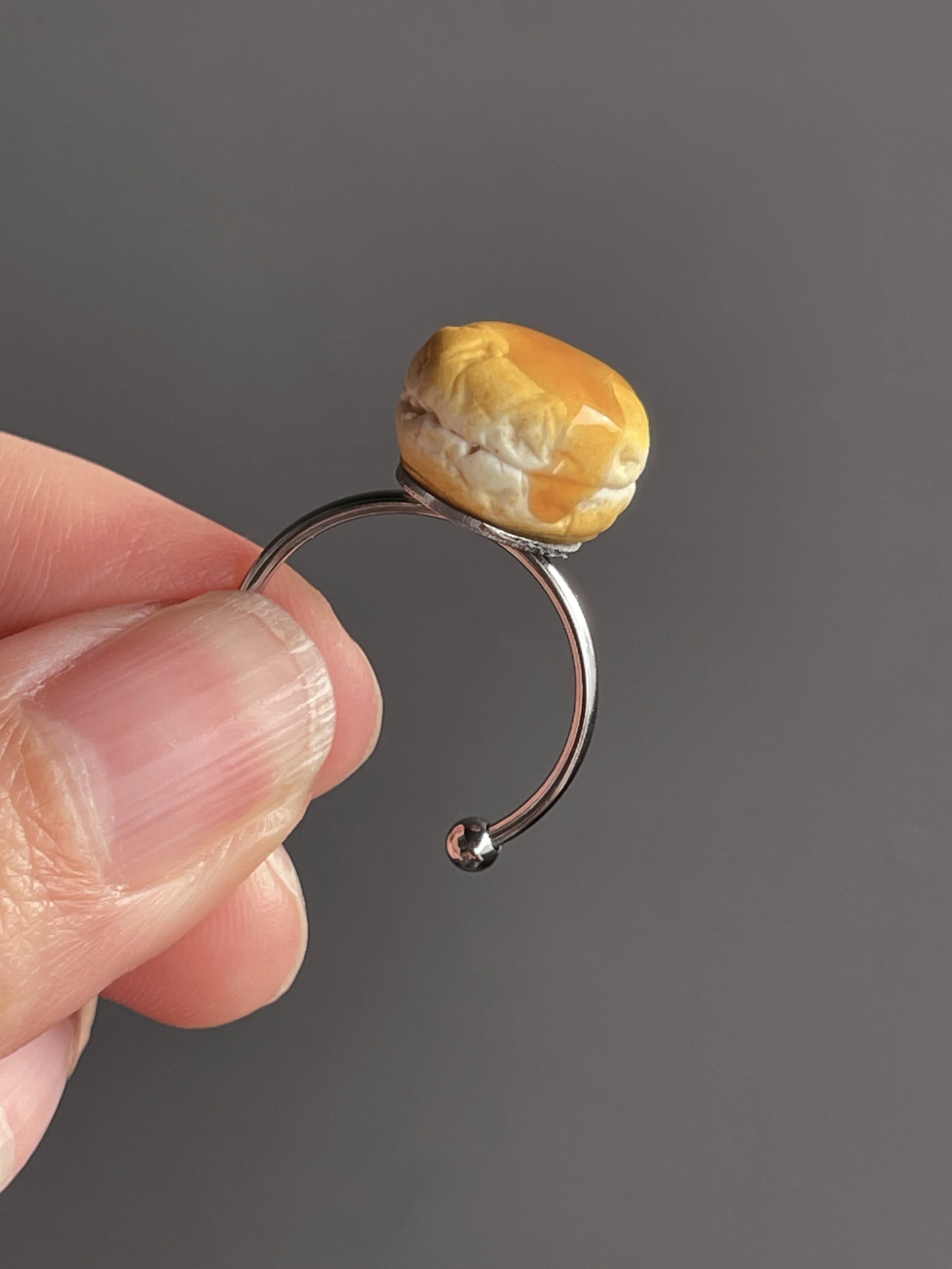 Fingers holding an adjustable ring topped with a miniature polymer clay biscuit with resin dripping honey.