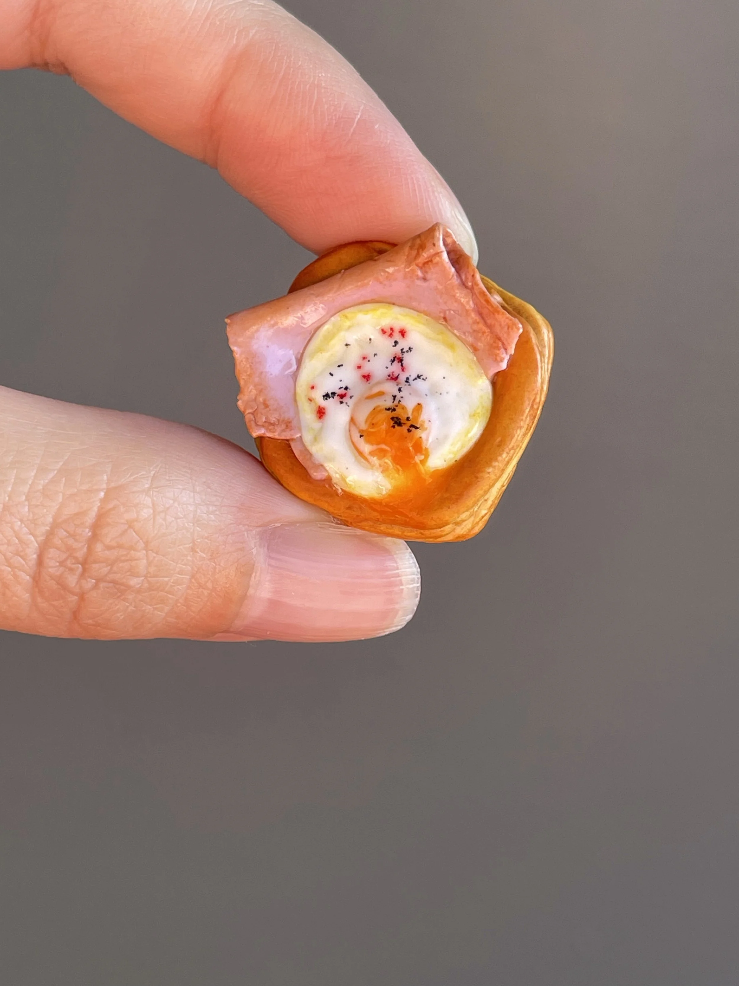 Fingers holding a miniature realistic polymer clay ham and egg danish magnet.