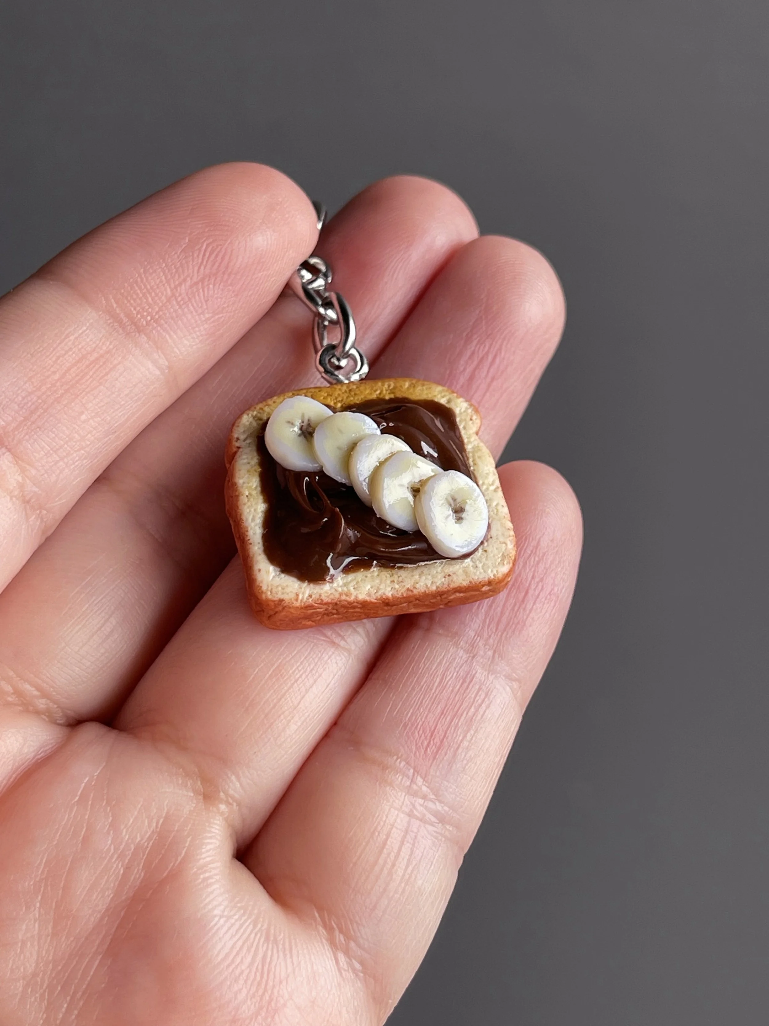 A hand holding a miniature polymer clay toast with hazelnut spread and banana slices.