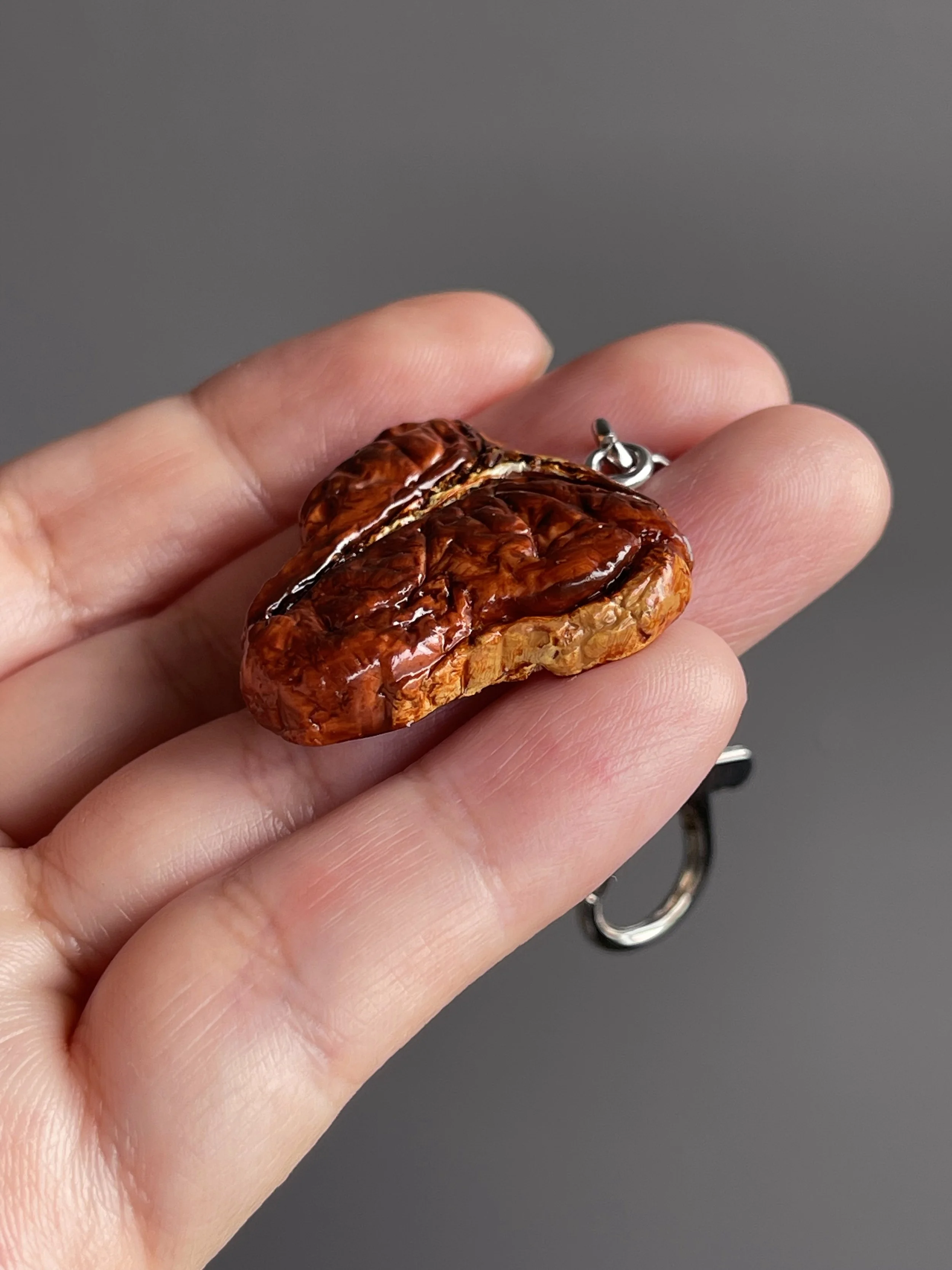 A hand holding a realistic miniature polymer clay t-bone steak keychain.