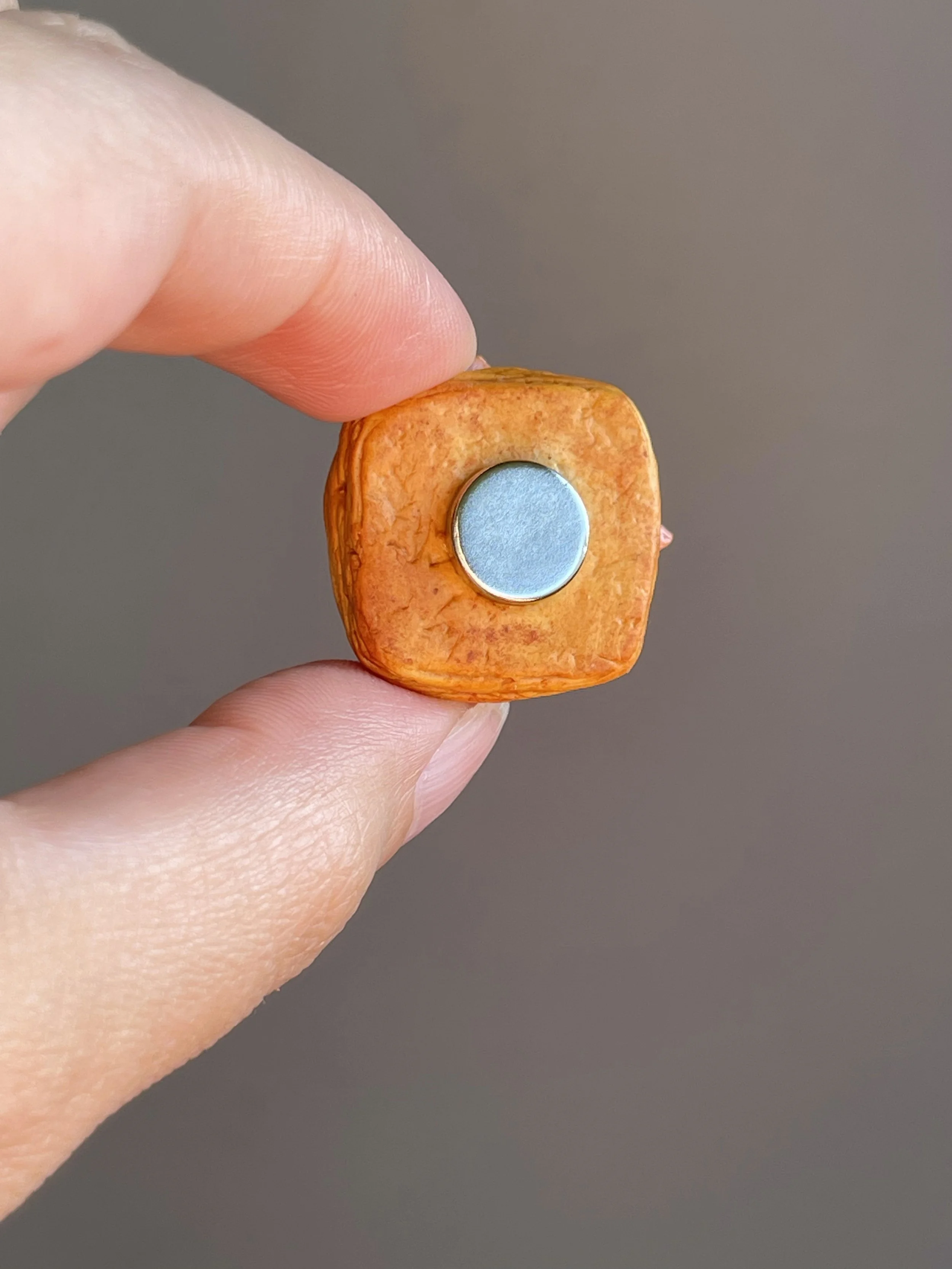 Fingers holding a miniature realistic polymer clay ham and egg danish magnet showing the back.