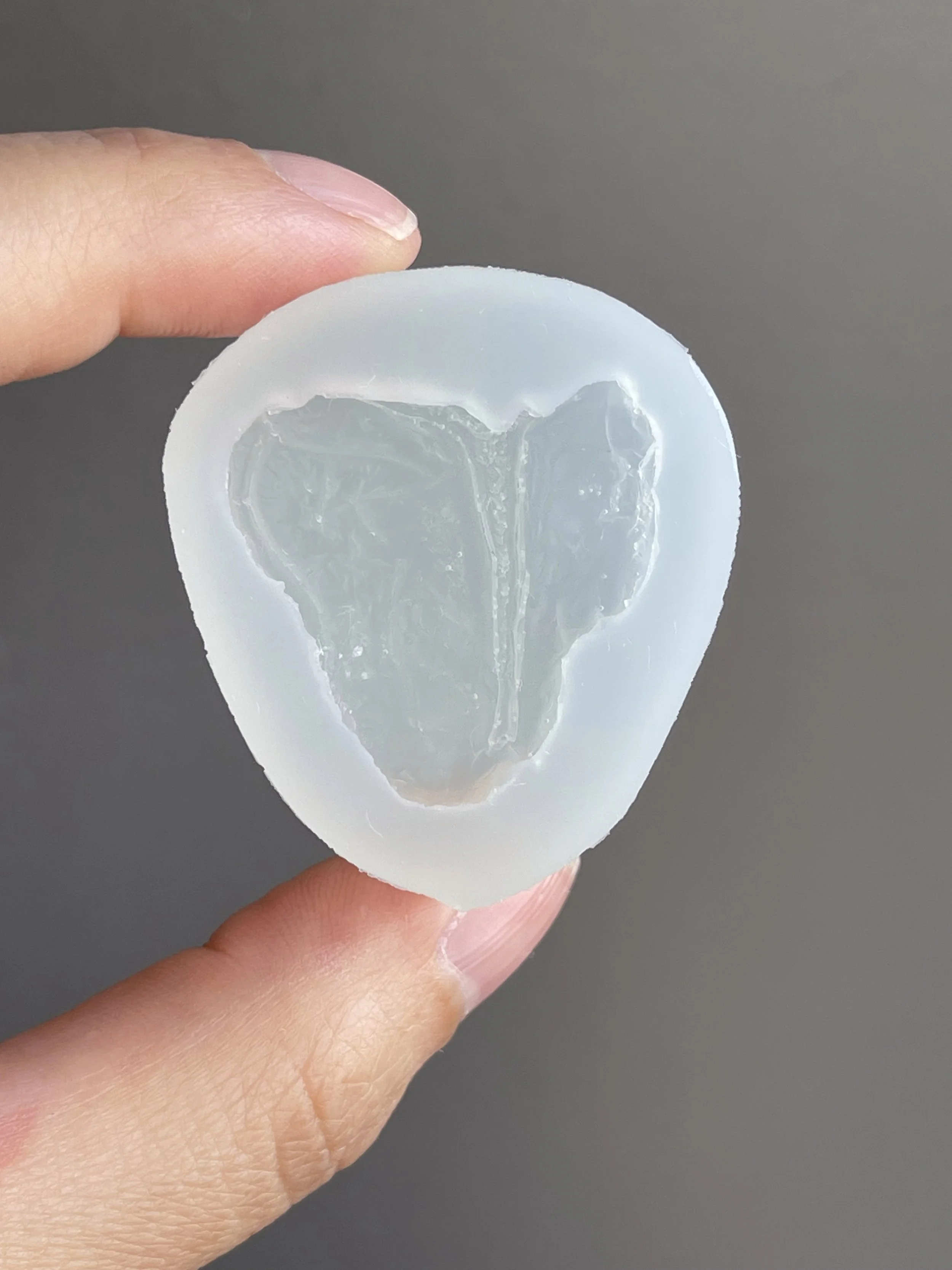 Fingers holding a t-bone steak clear silicone mold.