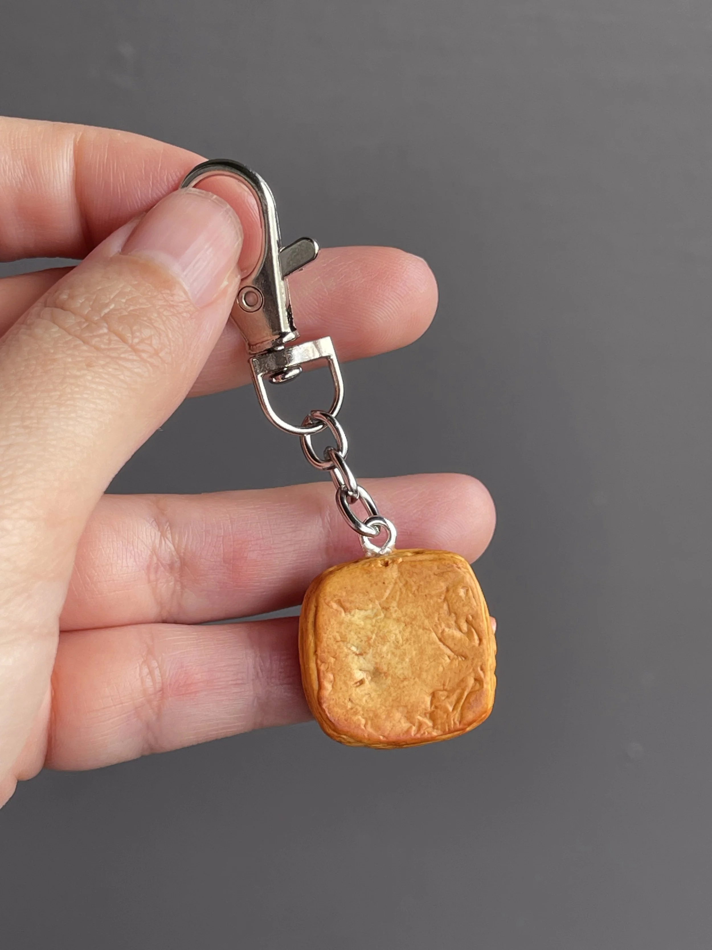 A hand holding a miniature polymer clay danish keychain showing the back of the piece.