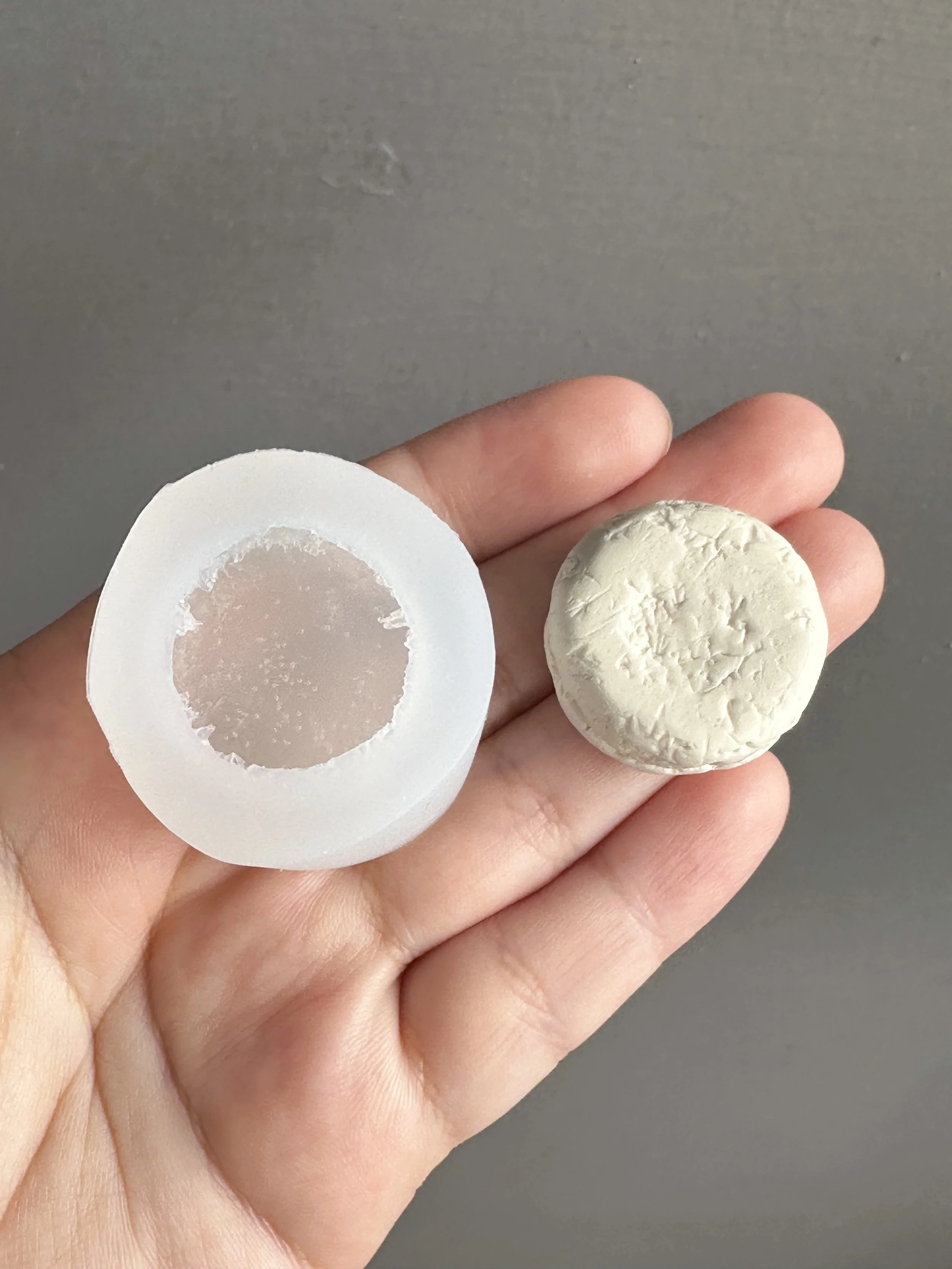 A hand holding a biscuit silicone mold with the master copy of the mold next to it.