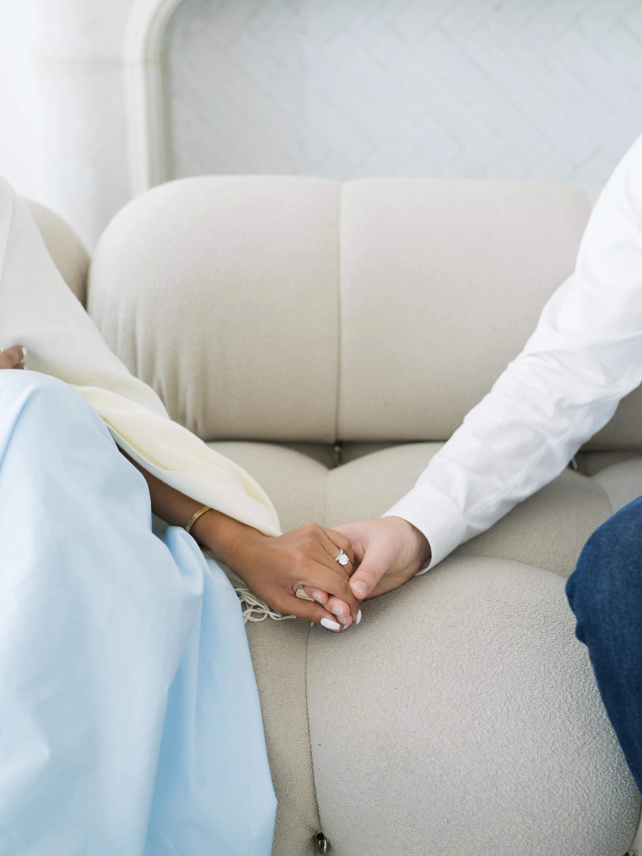A couple holding hands on a beige sofa during a visit to a counseling or therapy session.