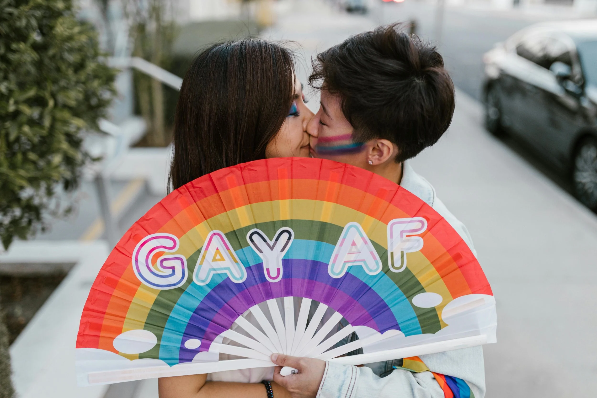 Zwei queere Personen mit Regenbogenfächer als Symbol für queersensible Psychotherapie und sichere therapeutische Räume.