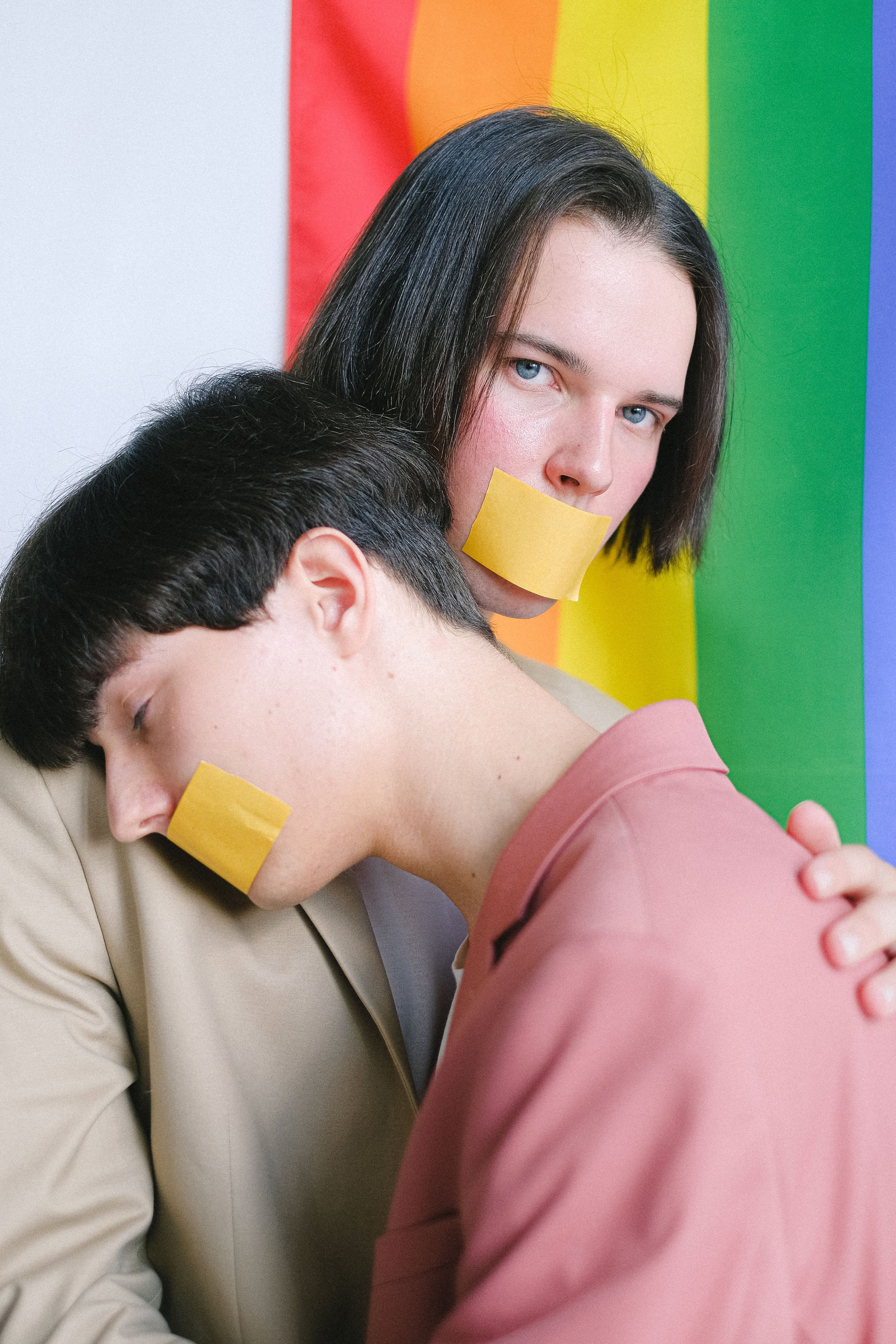 Porträt einer Person mit zugeklebtem Mund vor Regenbogenfarben als Symbol für Diskriminierung, Unsichtbarkeit und den Wunsch nach sicheren therapeutischen Räumen.