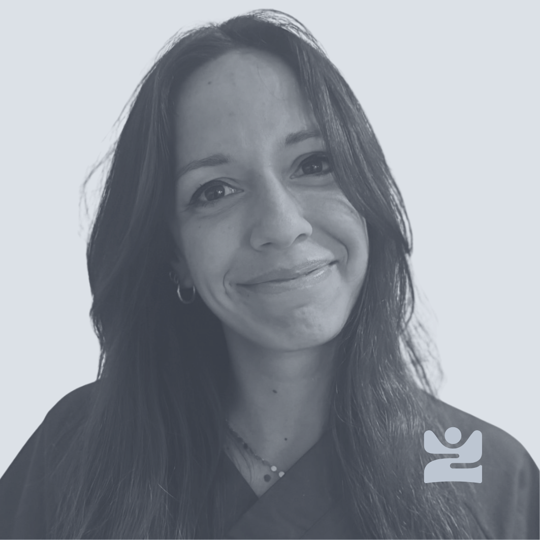 Ritratto di una donna sorridente con capelli lunghi e scuri, indossa orecchini e collana, sfondo chiaro.