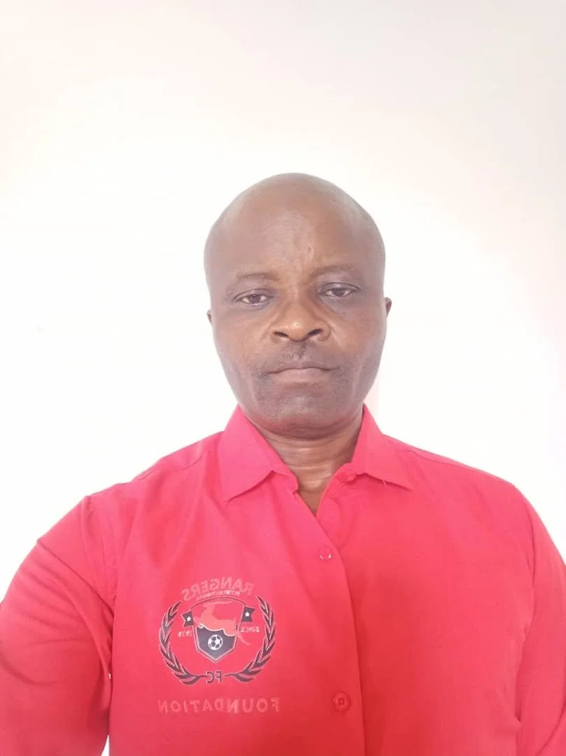 A man with a shaved head wearing a red shirt with a logo on the left side, posing against a plain white background.