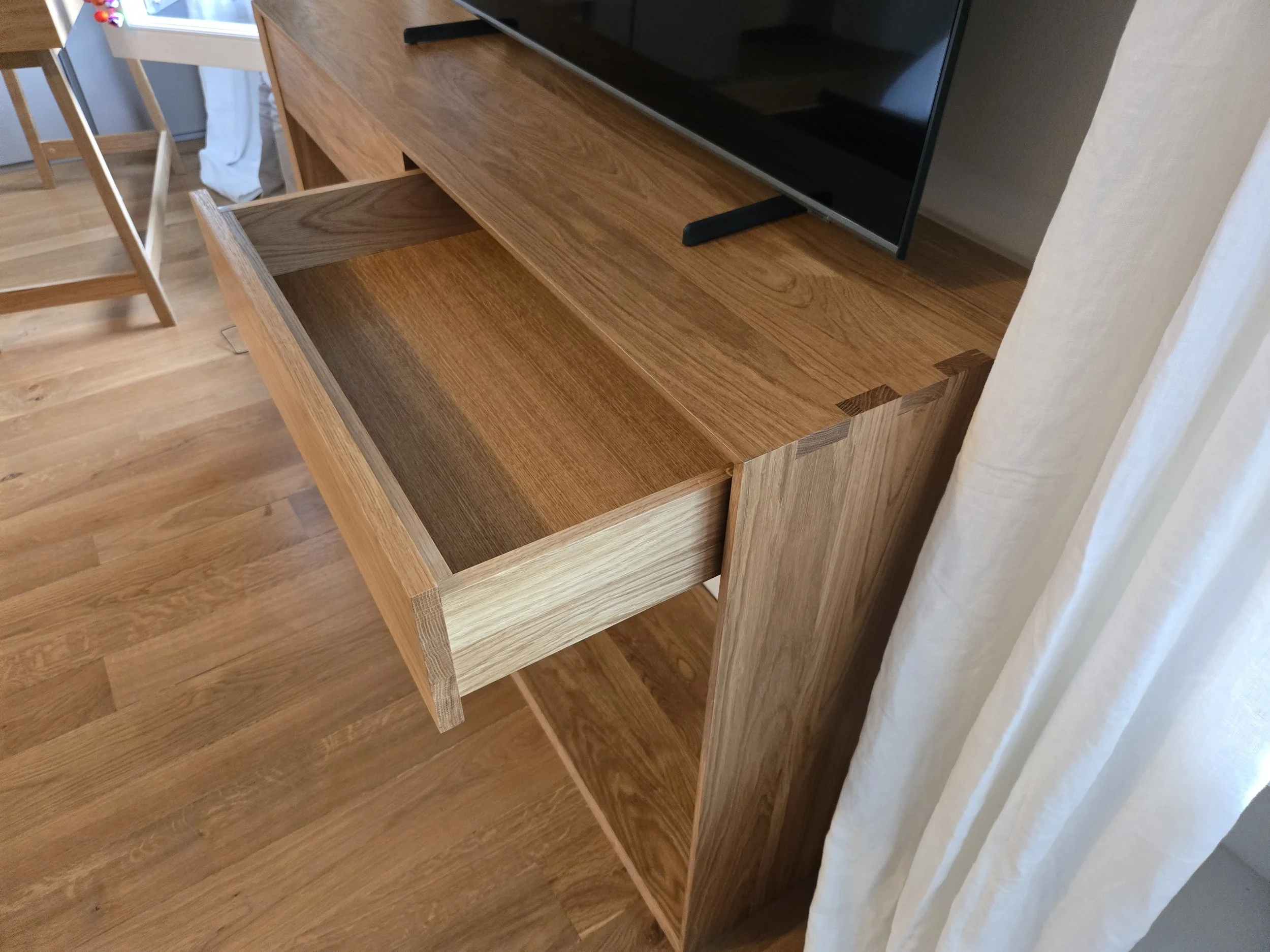 Meuble TV en chêne massif avec queues droites et raccord à l'onglet. Fabrication artisanale sur mesures pour inclure les prises électriques dans l'espace sous les tiroirs. Dos amovible à peindre pour cacher les prises. Tiroirs en chêne massif. Créden