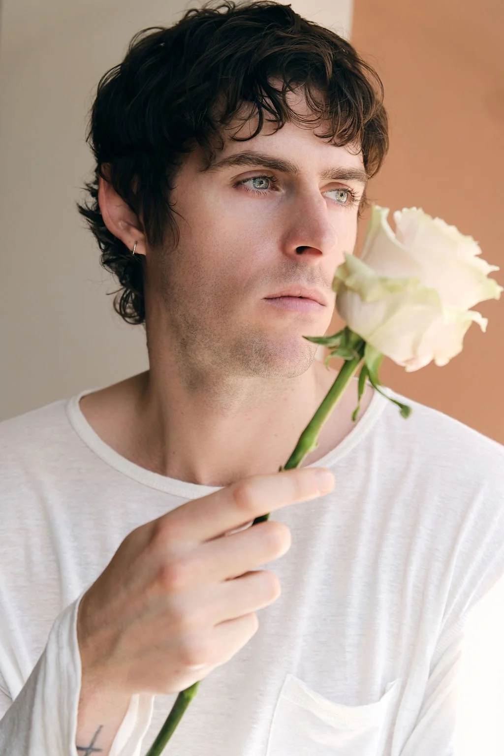 A man holding a white rose over his face, while looking sideways into the distance
