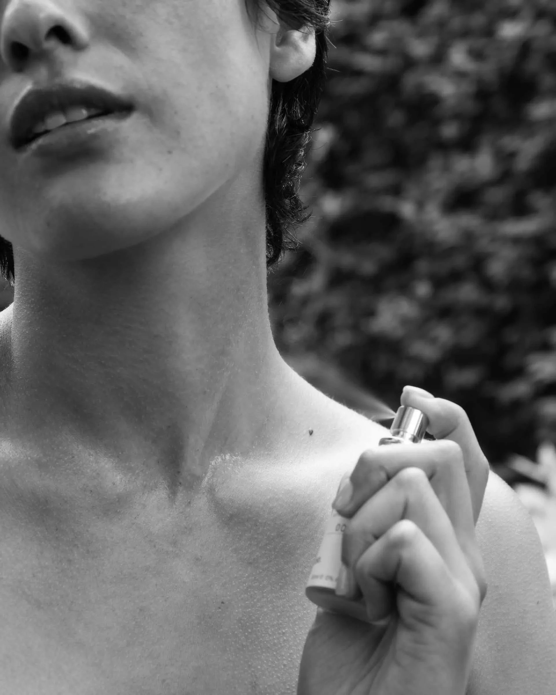 Closeup B&W image of Prem Rouge fragrance being sprayed on the neck of a woman.