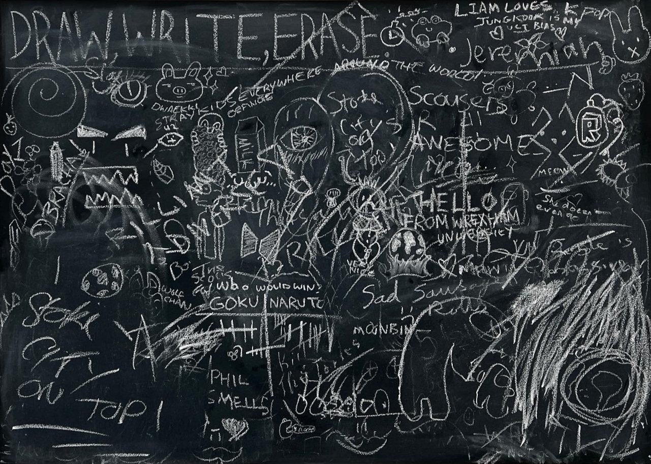 A chalkboard filled with various doodles, drawings, and handwritten notes, including characters, shapes, and phrases such as 'Draw, Write, Erase'.