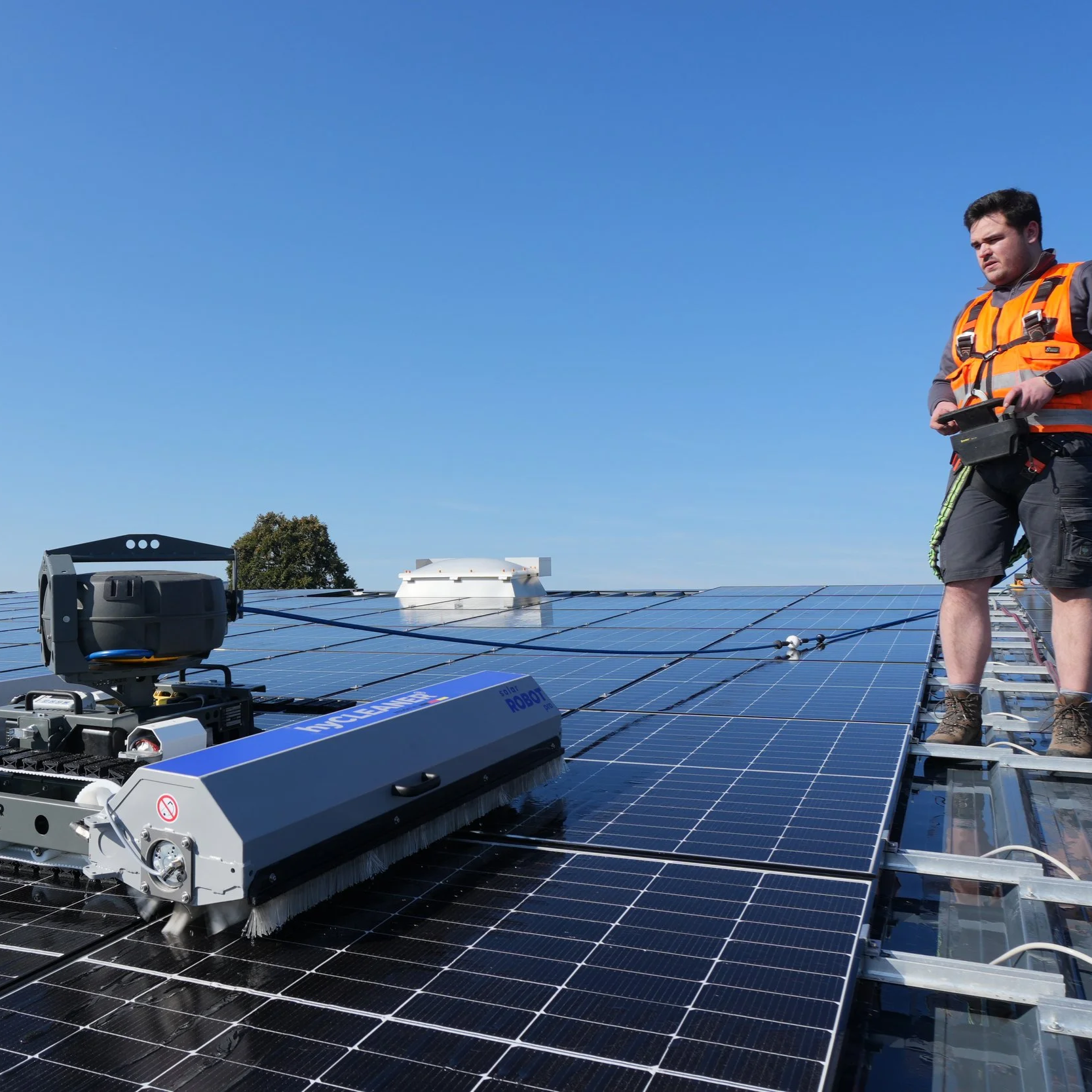 Fachkraft für Solarreinigung, reinigt mit Roboter Solarpanels auf einer Dachfläche.