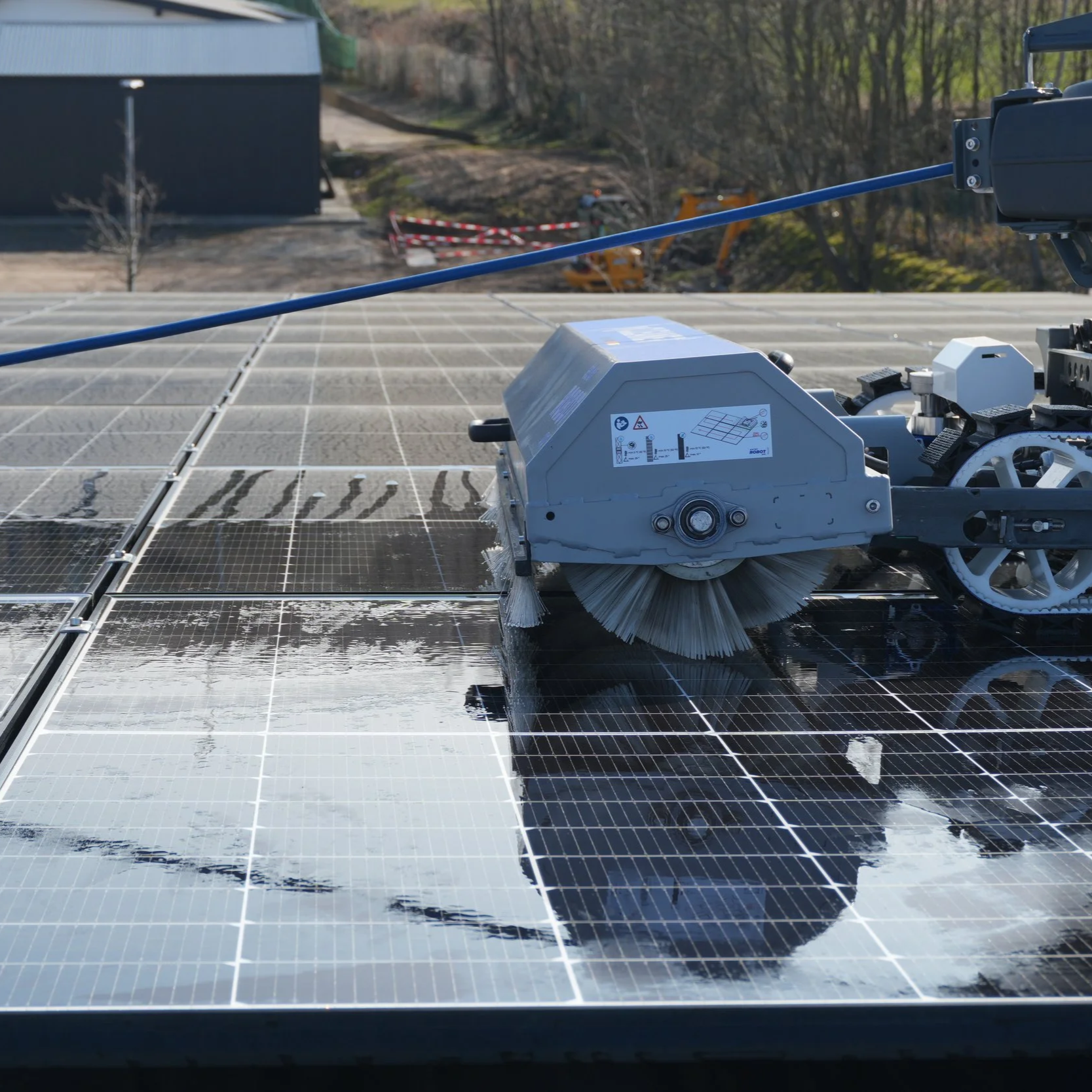Nahaufnahme eines Reinigungsroboters auf einer Solaranlage, die den deutlichen Unterschied zwischen verschmutzten und bereits gereinigten Modulflächen zeigt.