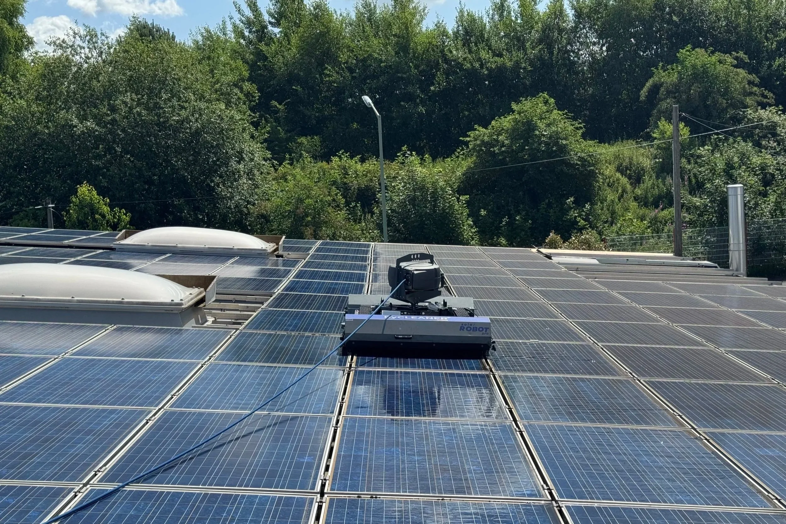 Ein Solarreinigungsroboter reinigt eine Photovoltaikanlage auf einem Dach und zeigt den deutlichen Unterschied zwischen verschmutzten und bereits gereinigten Solarmodulen. Die professionelle Solarreinigung sorgt für ein sichtbar sauberes Ergebnis und