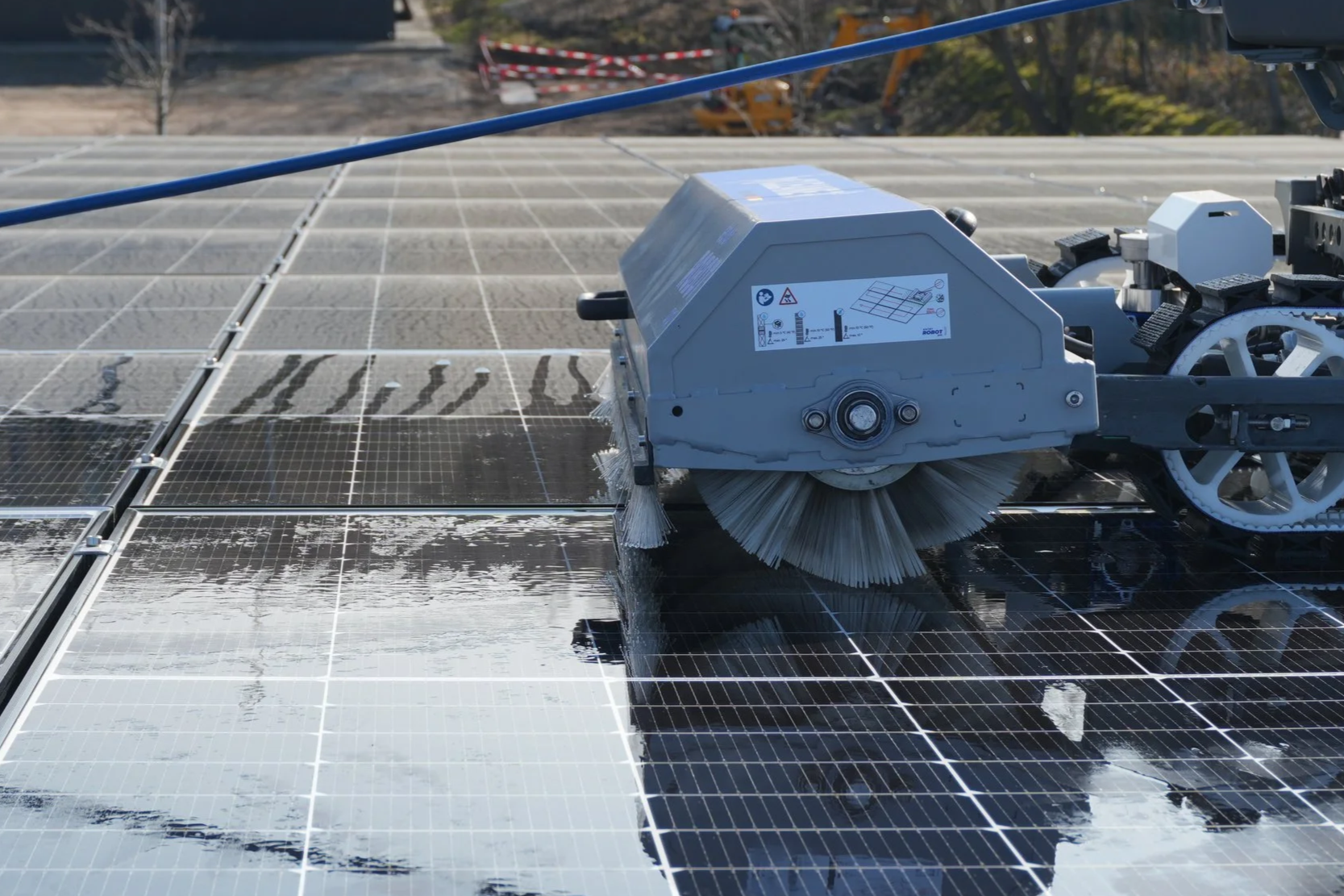 Nahaufnahme eines Reinigungsroboters auf einer Solaranlage, die den deutlichen Unterschied zwischen verschmutzten und bereits gereinigten Modulflächen zeigt.