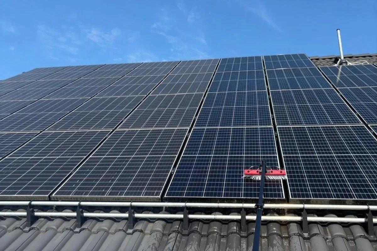 Solaranlage auf einem Hausdach, Reinigungsgerät in Verwendung, blauer Himmel
