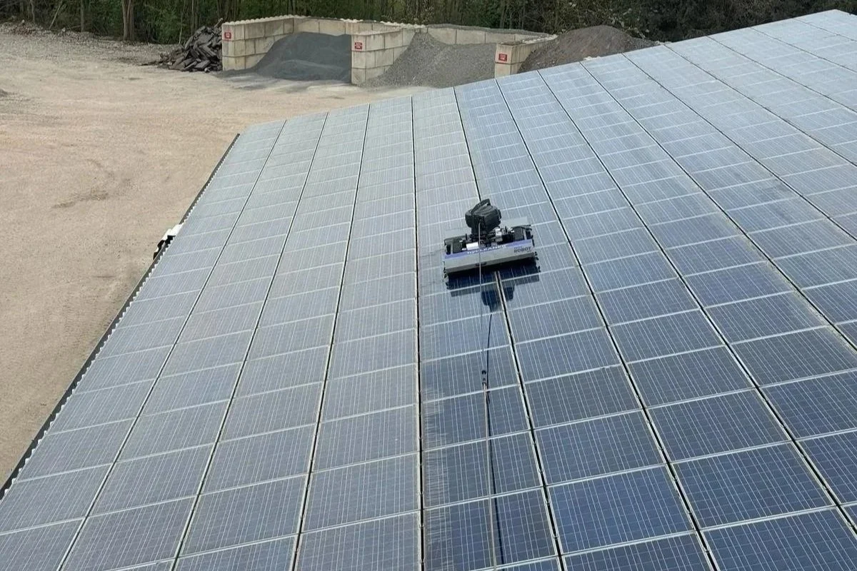 Photovoltaikanlage mit Solarmodulen auf einem Gebäude, in einer ländlichen Umgebung mit Bäumen und Hügeln im Hintergrund.