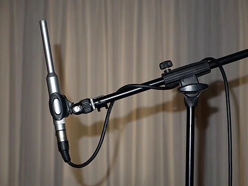 Condenser microphone on a boom stand with a beige curtain background