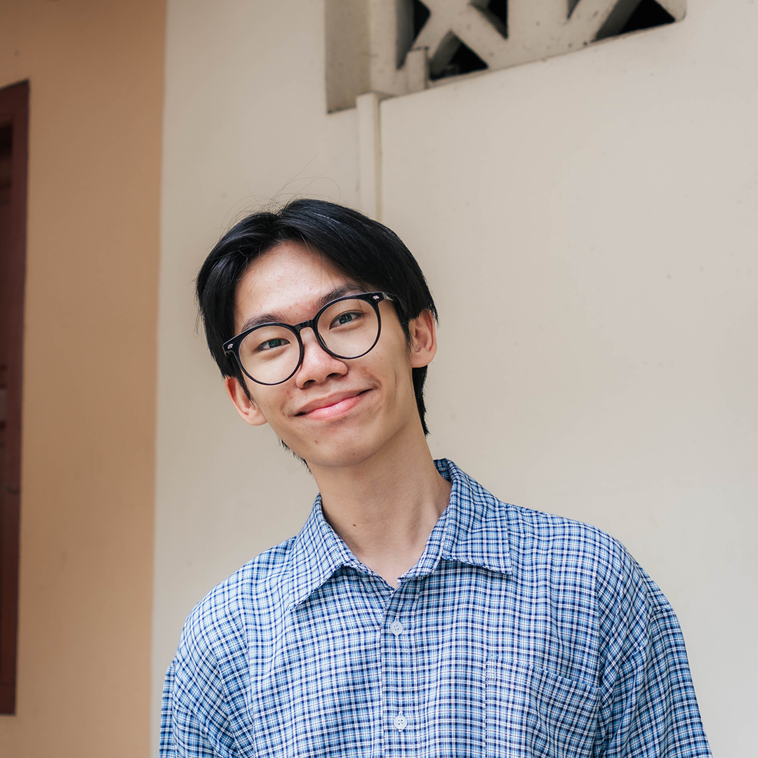 Person wearing glasses and a blue checkered shirt, smiling against a beige background.