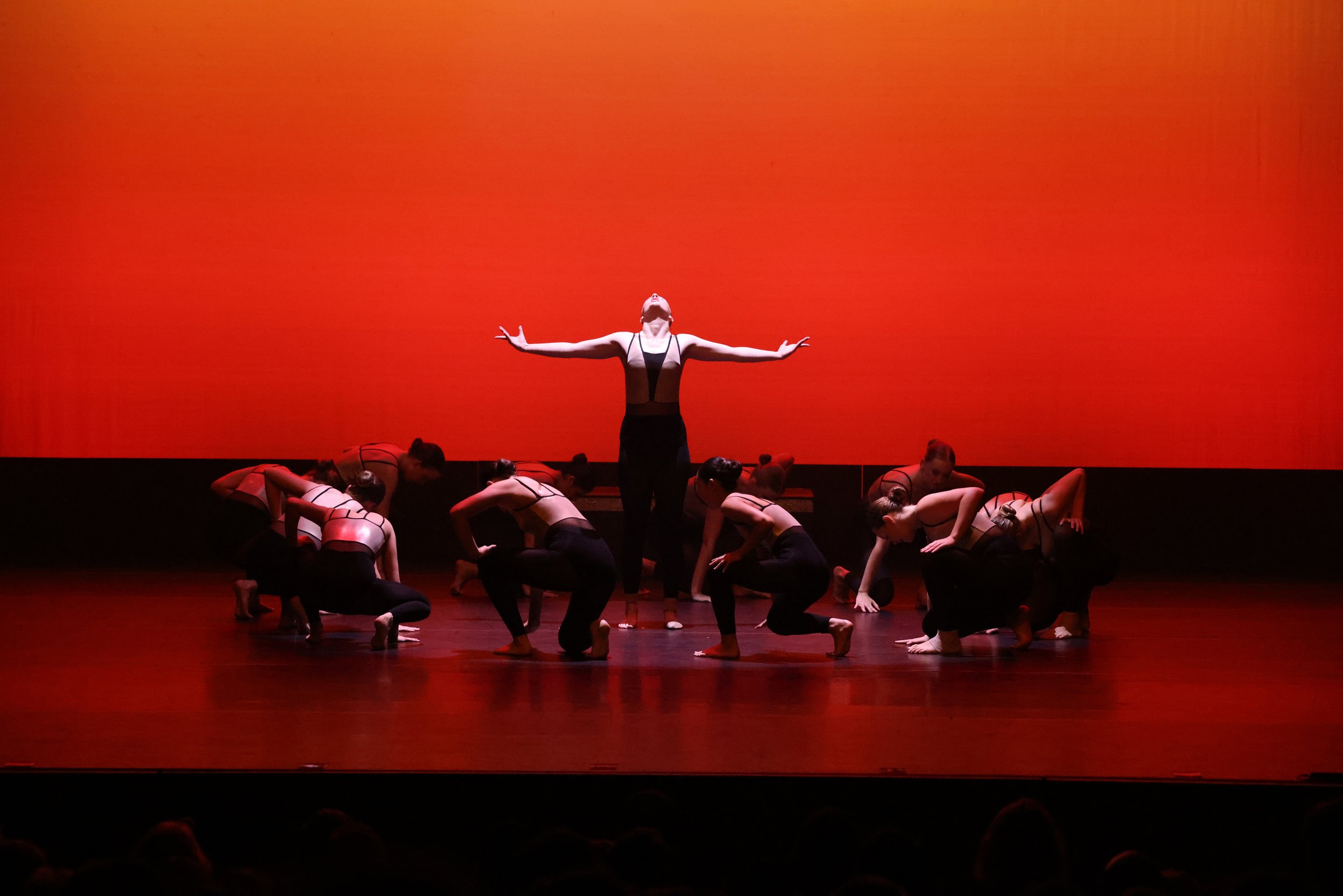 group of dancers crouching down on stage and one dancer standing in center