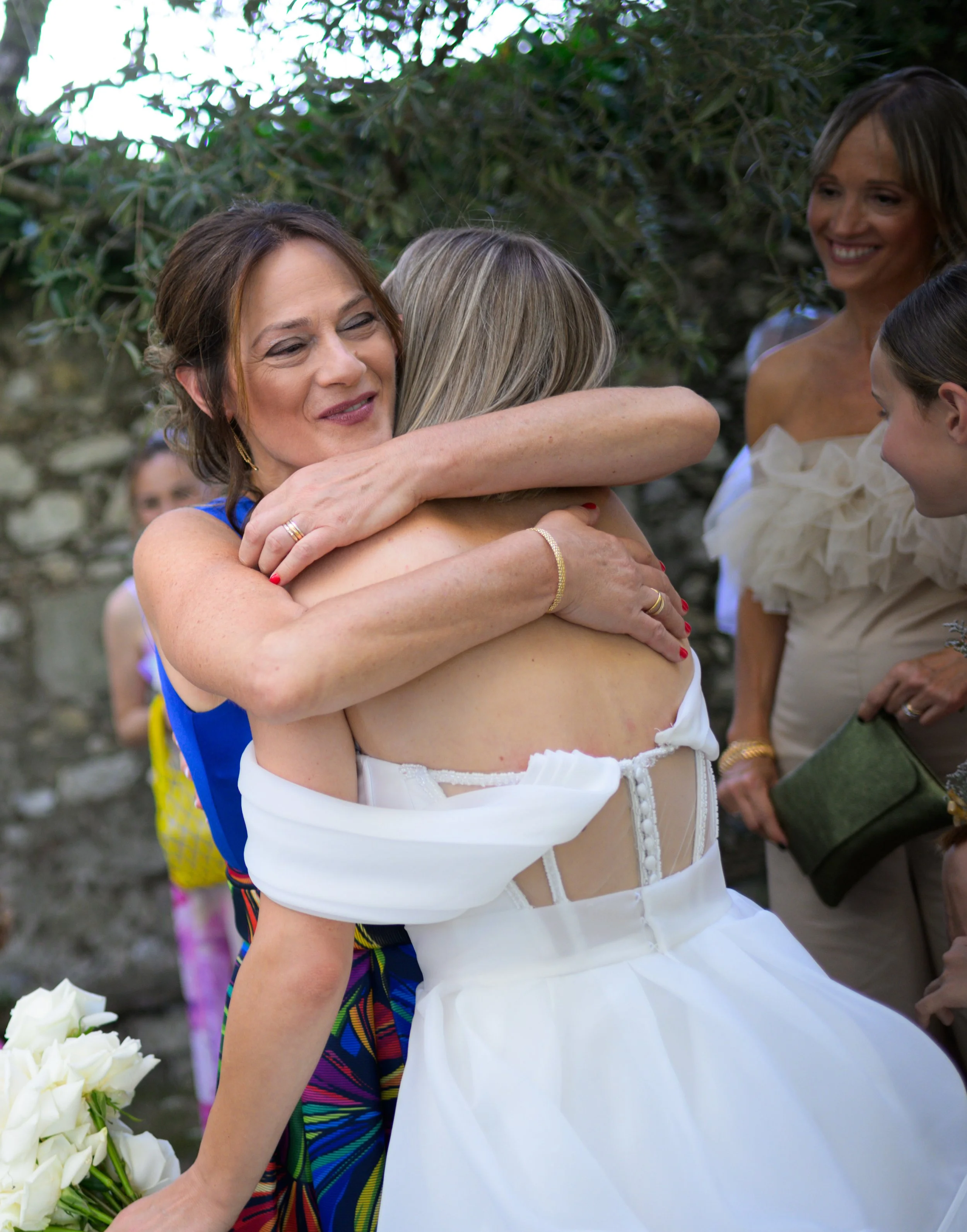 Donna che abbraccia una sposa con altre persone in una scena all'aperto.