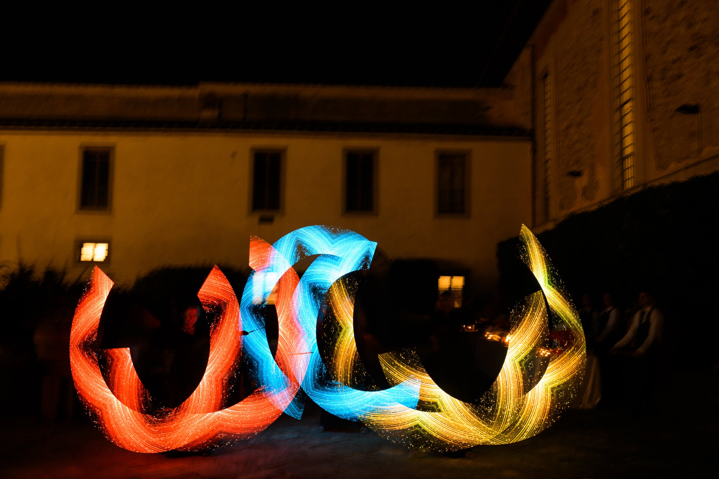 Scie luminose multicolori in movimento davanti a un edificio notturno.