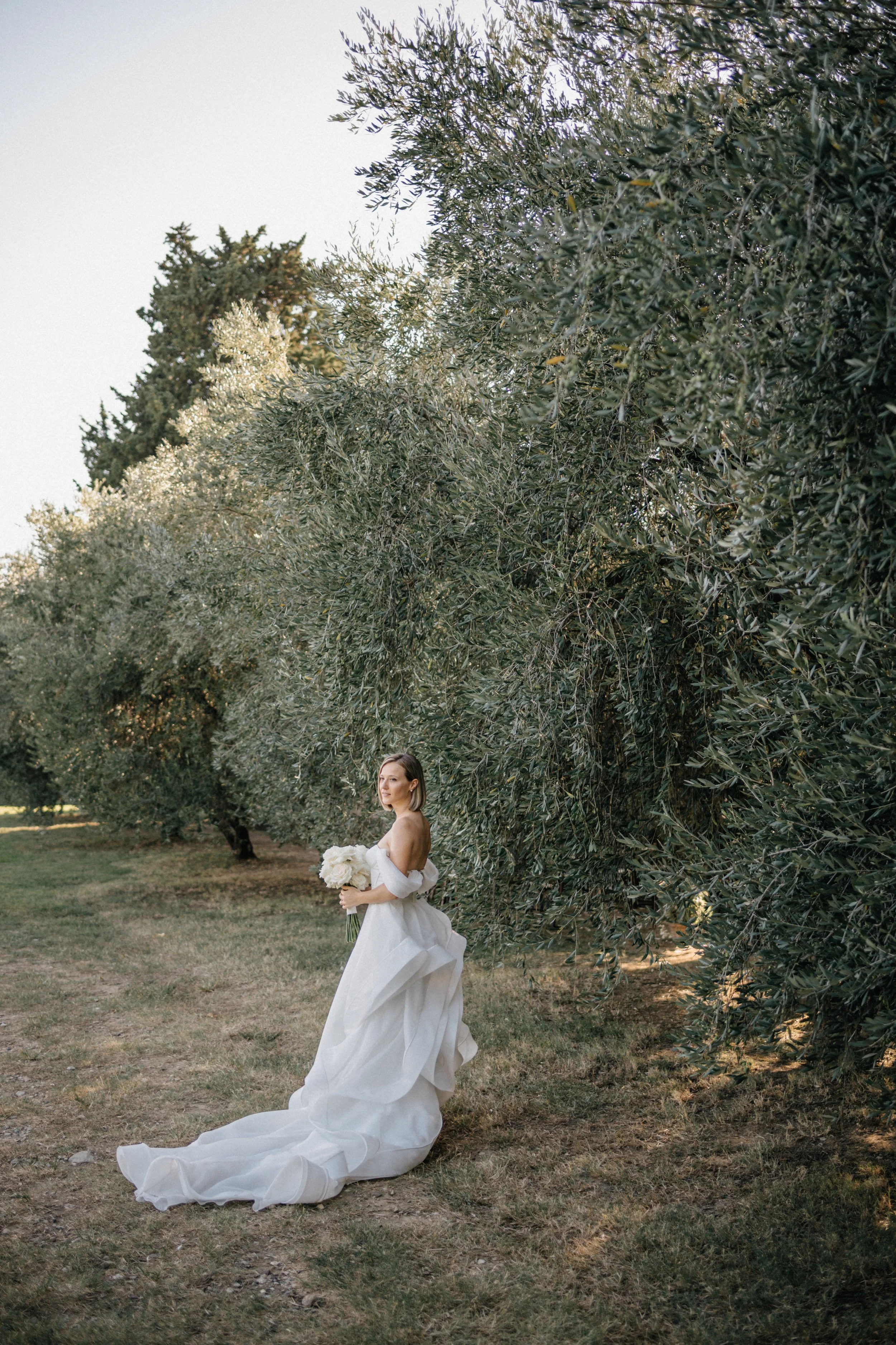 Sposa con abito bianco e bouquet in un giardino con alberi.
