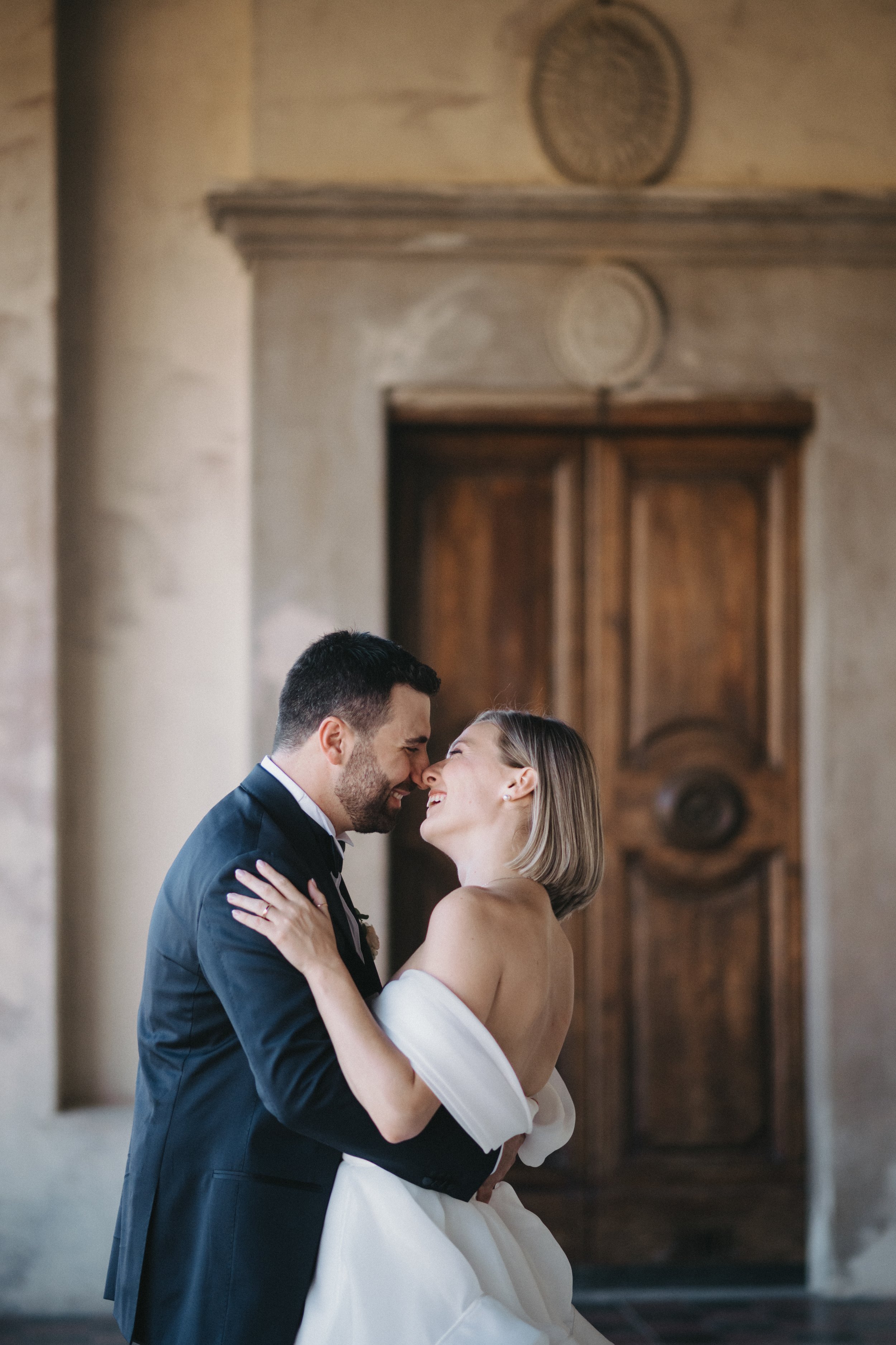 Coppia di sposi sorridenti che si abbracciano davanti a una porta in legno.