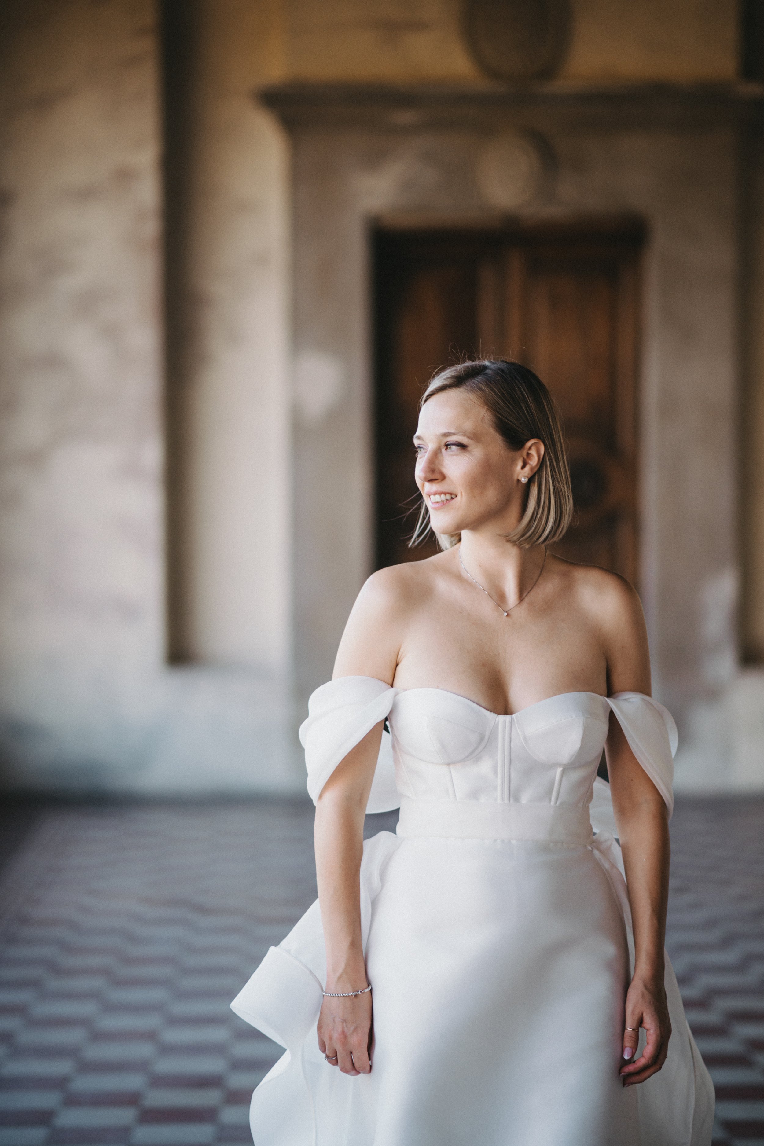 Donna in abito da sposa bianco, con sfondo architettonico.