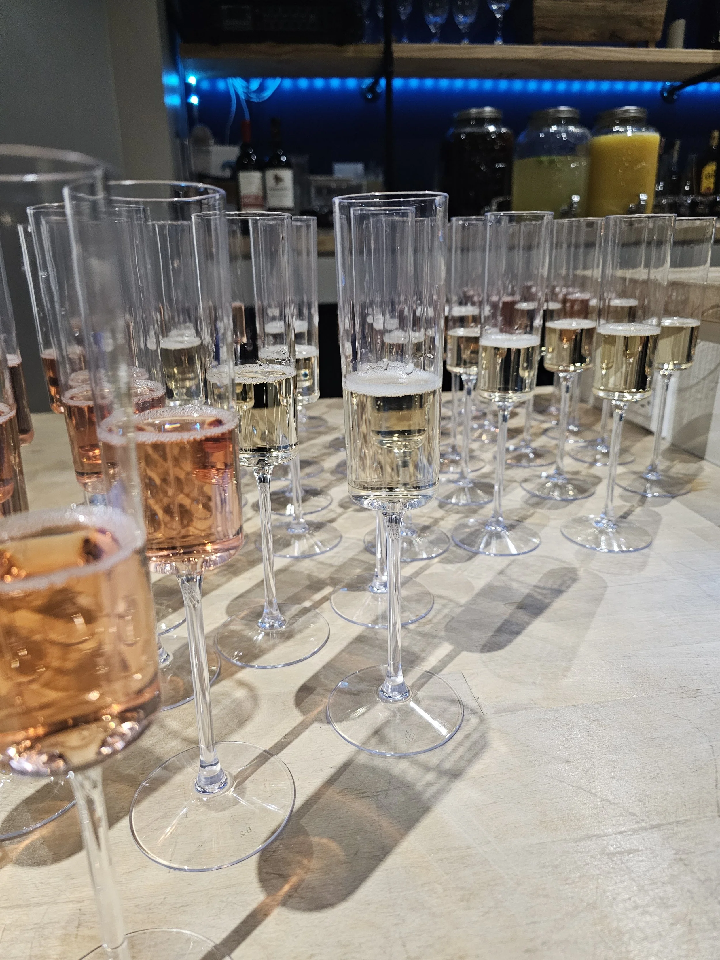 Multiple champagne flutes filled with pink, clear, and yellow sparkling wine on a wooden table.
