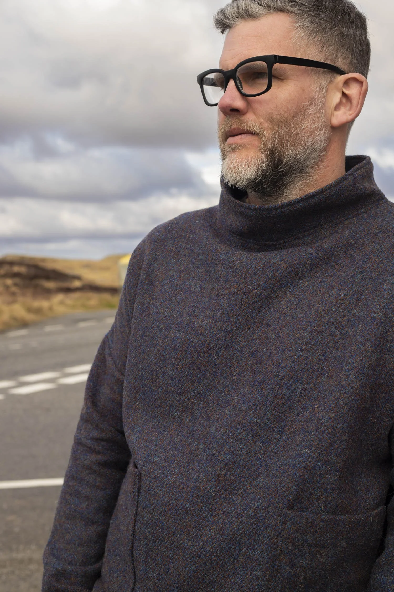 Man wears light grey smock and stand nexts to telegraph pole