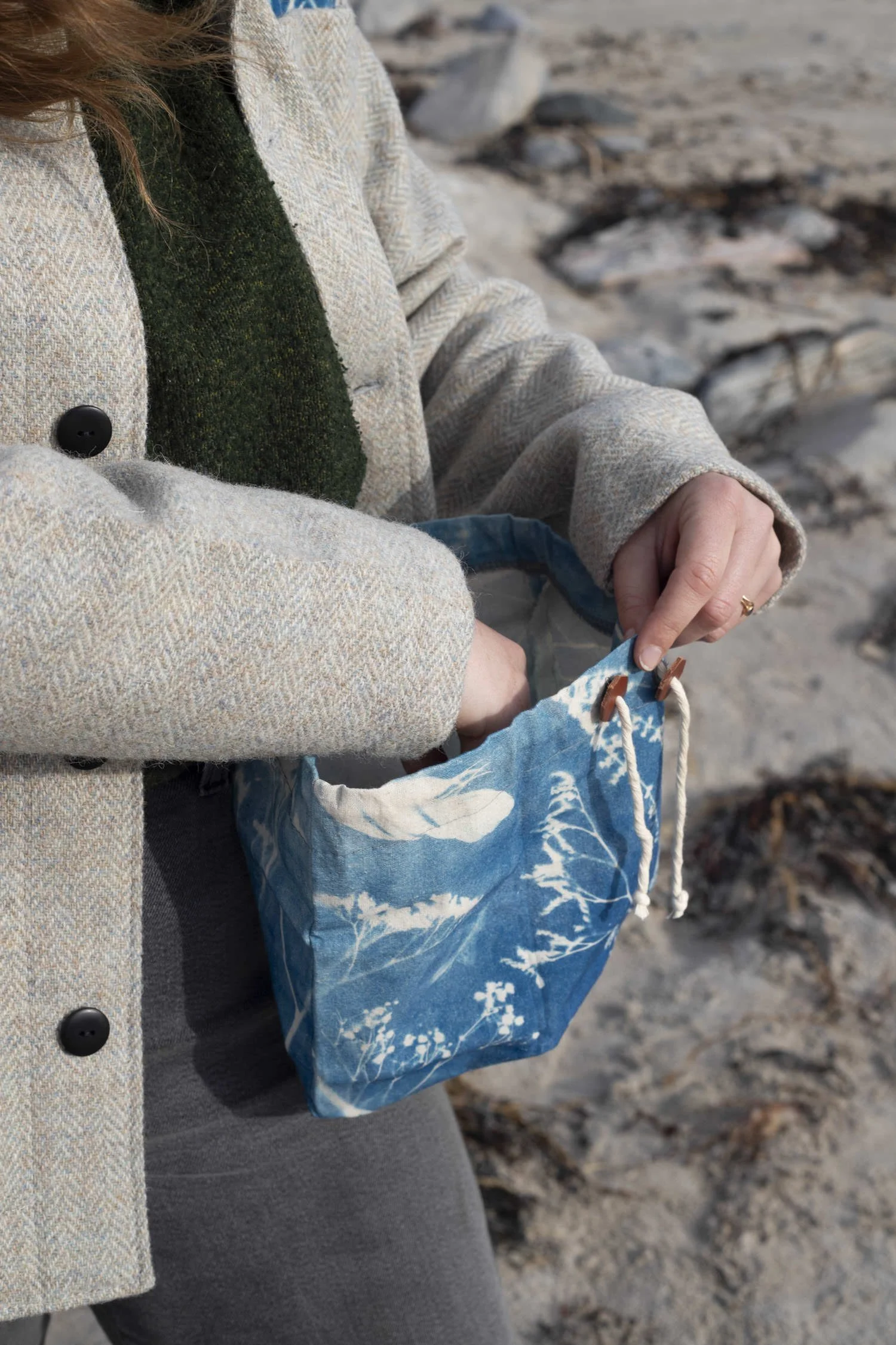 Hand reaching into a printed blue belt bag, a sandy beach in the background