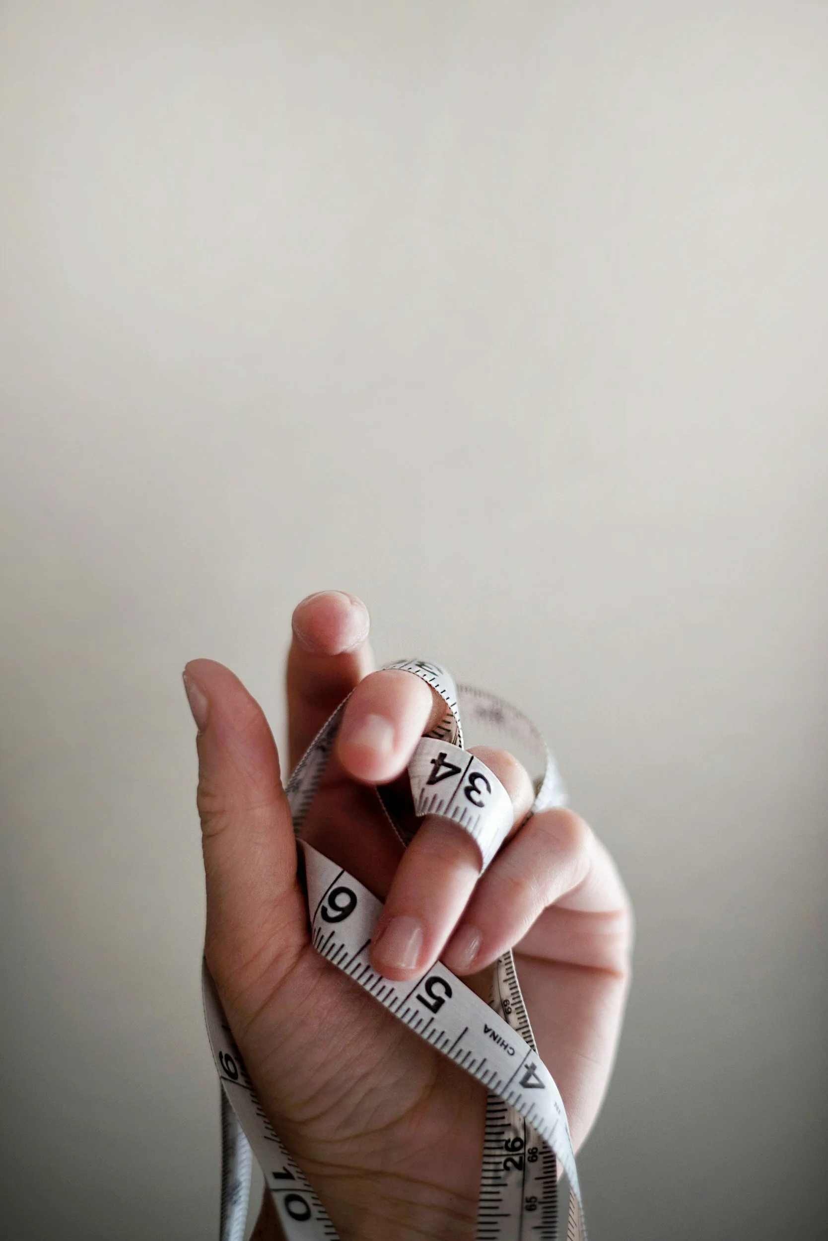 A hand holding a measuring tape with a plain light-colored wall in the background.