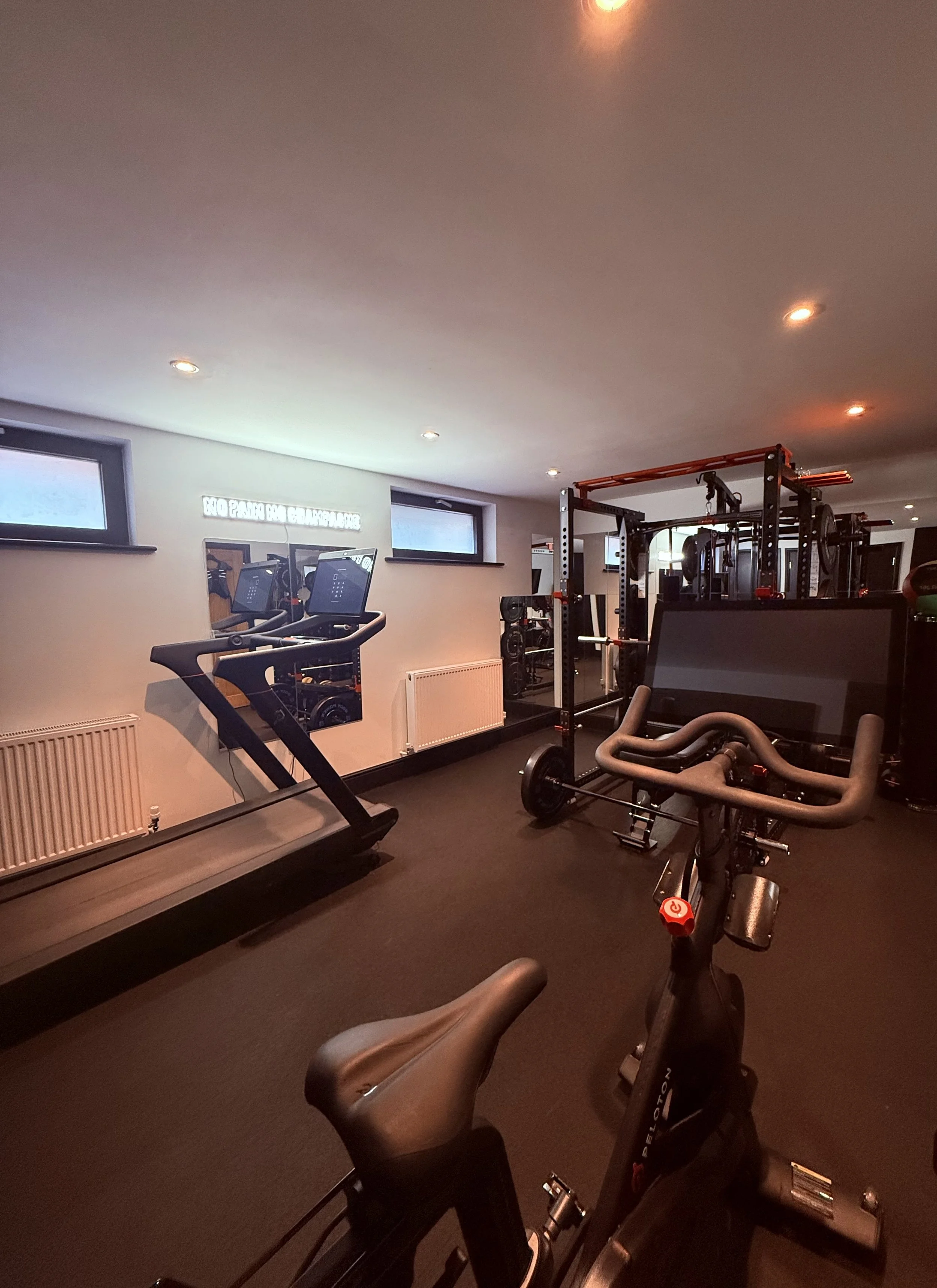 Home gym with treadmill, exercise bike, and weightlifting equipment in a room with small windows and ceiling lights.