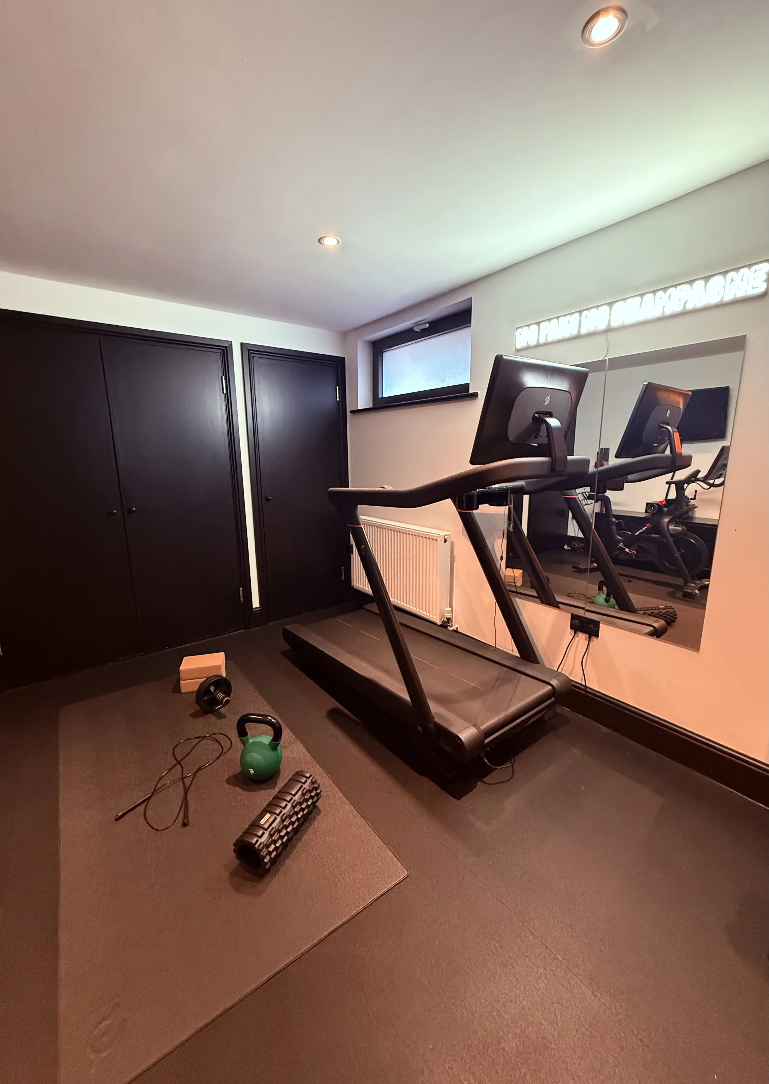 Home gym with a treadmill, weight equipment, and workout accessories, reflected in a mirror on the wall.