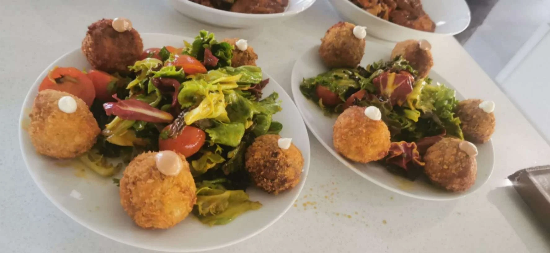 Plated mixed salad surrounded by golden croquettes with small dots of sauce.
