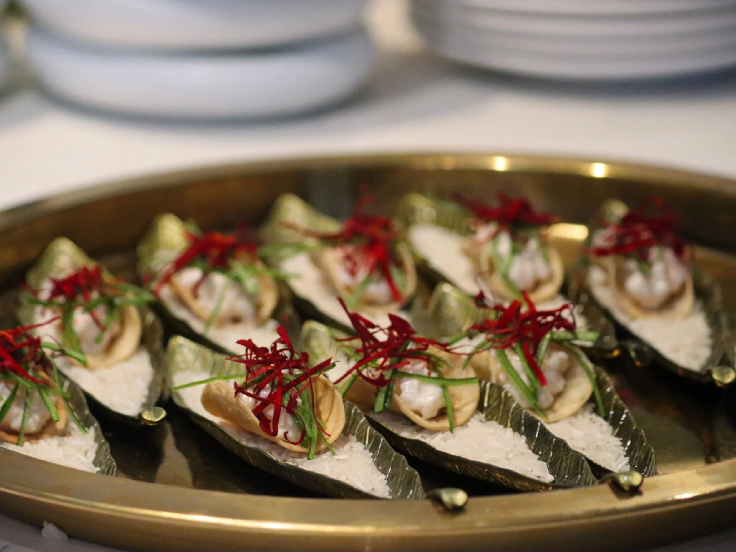 Platter of mini fine dining tacos with creamy filling, cucumber and red garnish.
