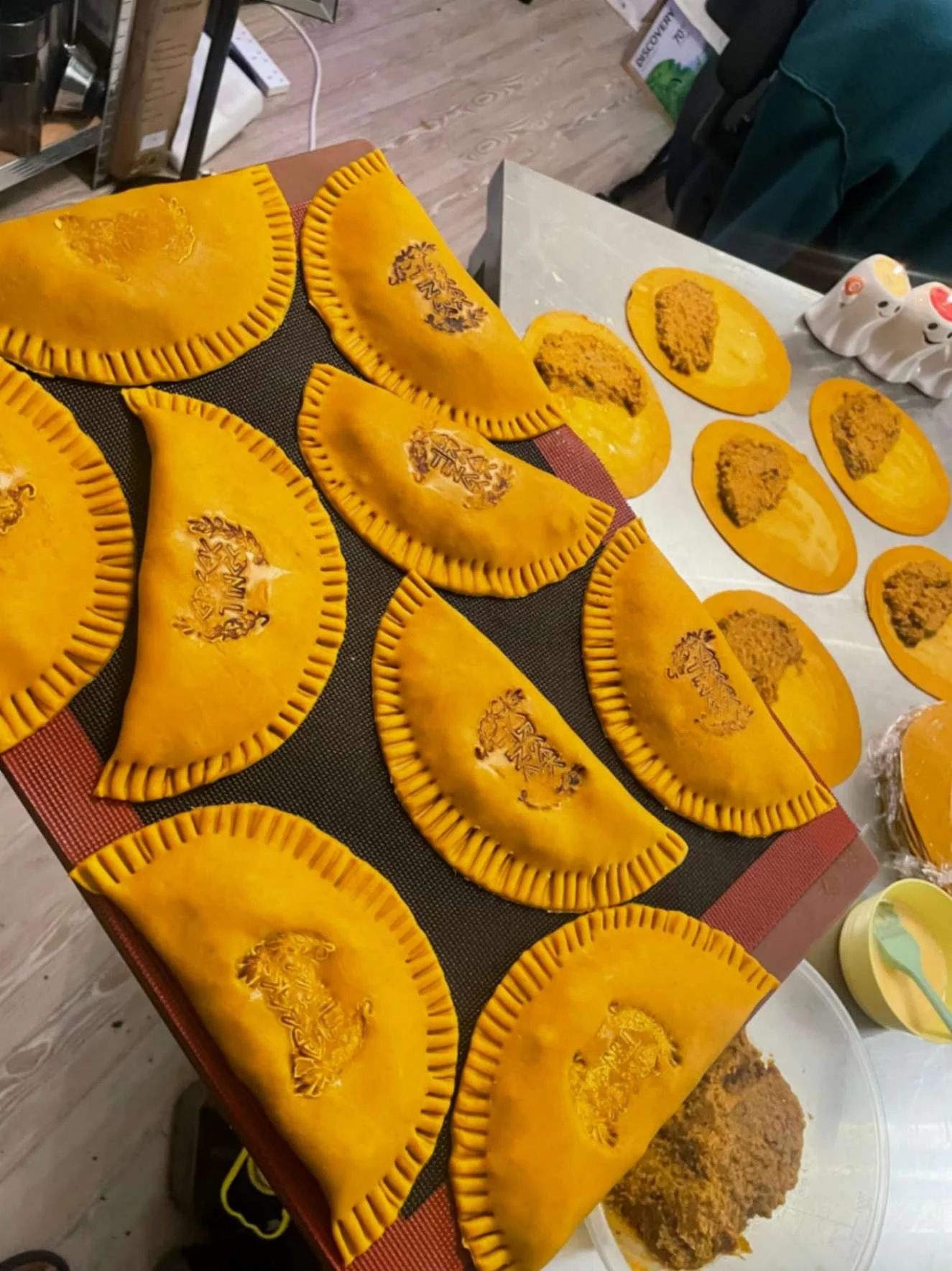 Rows of handmade golden Jamaican patties being filled and prepared in the Greek Tings kitchen.
