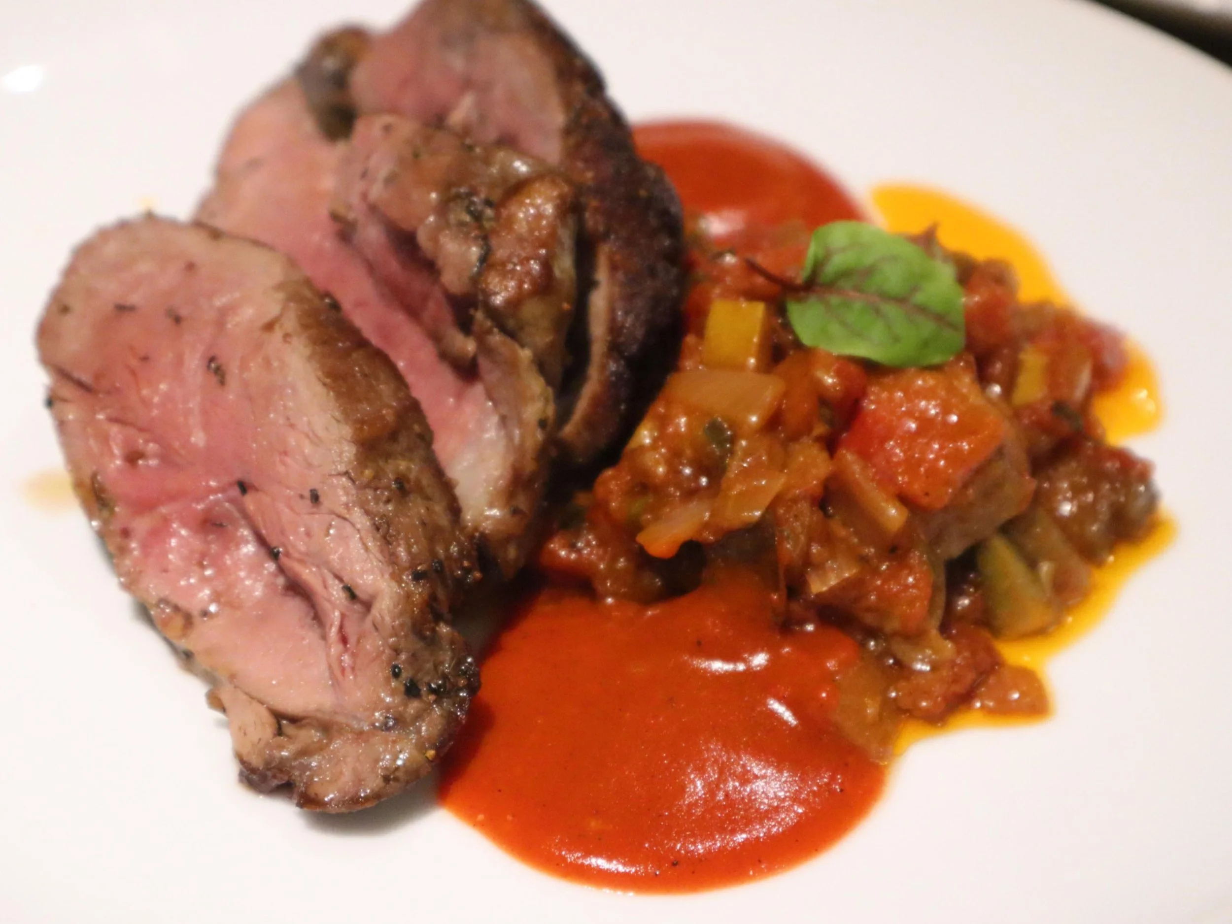 Roast lamb slices with colourful vegetables and rich sauce on a plated British menu.
