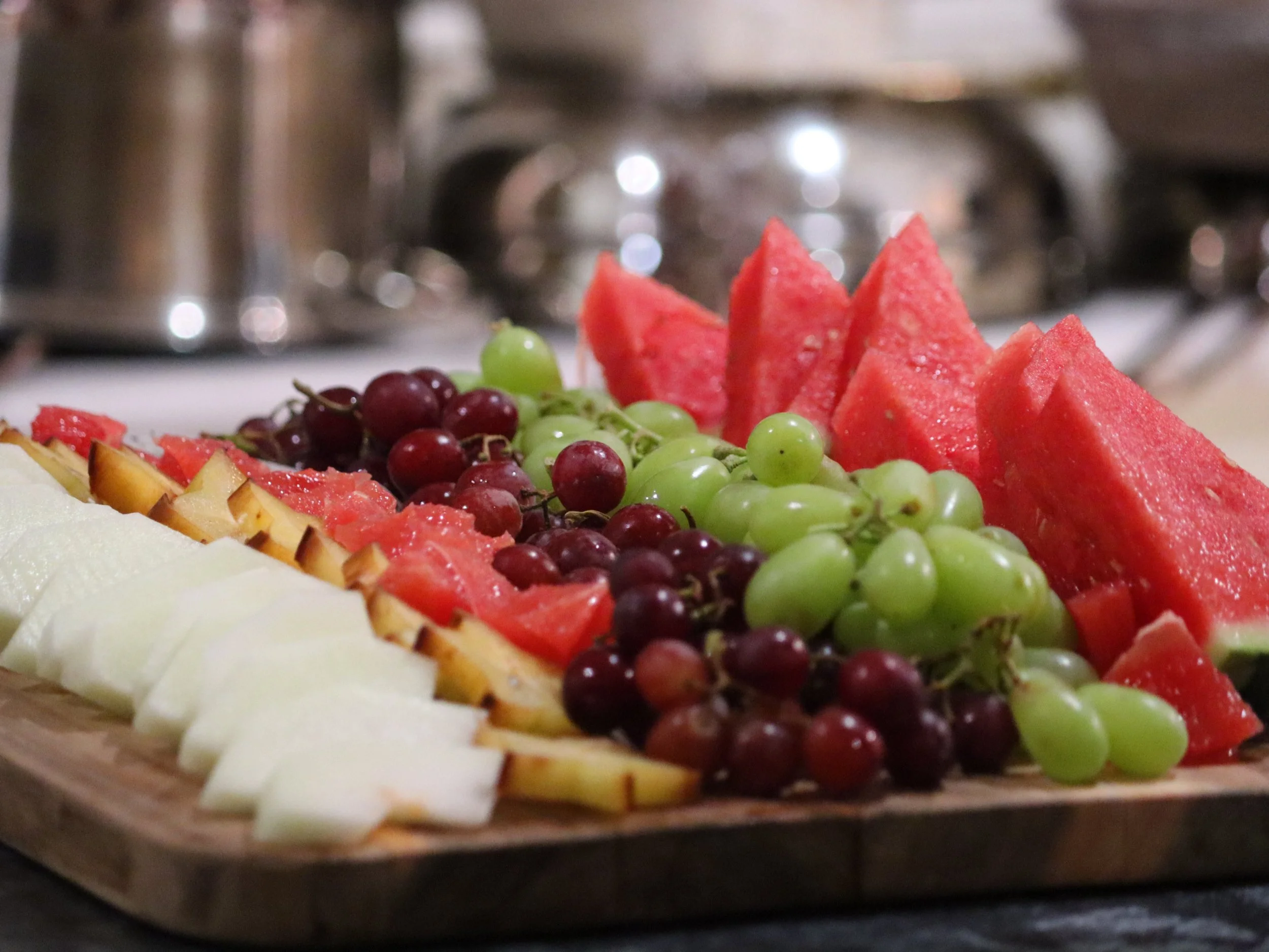 Fresh fruit platter, watermelon, red grapes, white grapes, starfruit, and honeydew melon in lines.