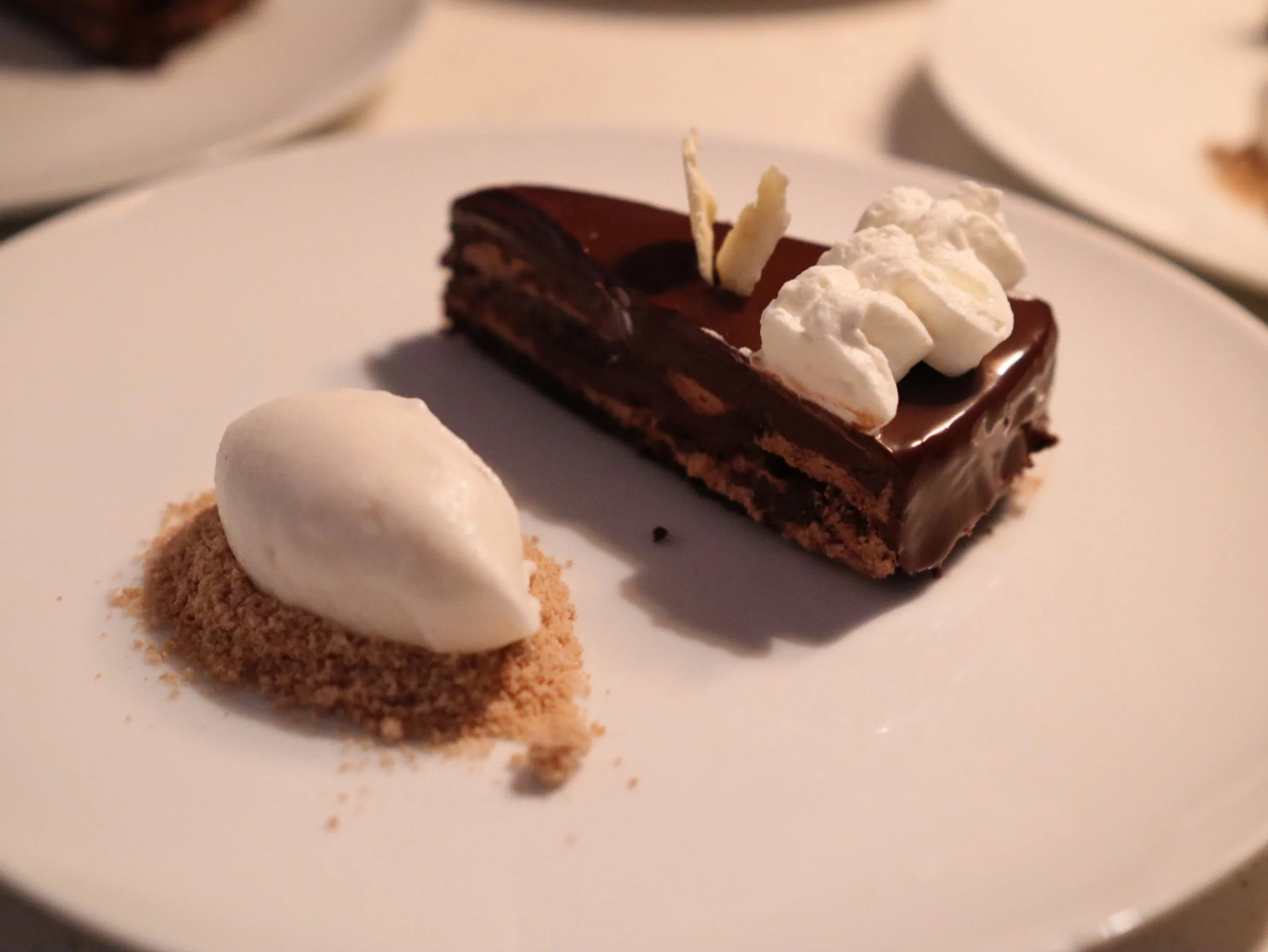 Chocolate layer cake with glossy glaze, whipped cream and a quenelle on biscuit crumb.
